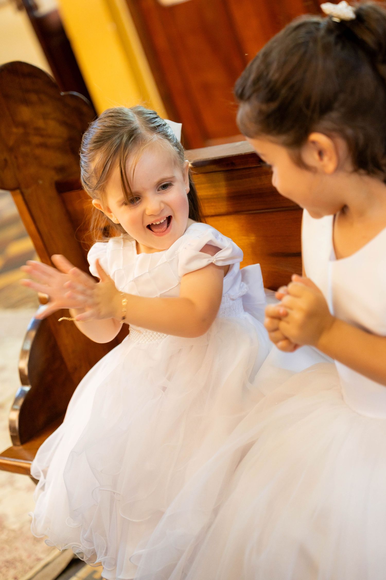 Two little girls in white dresses playing clapping games together, smiling and laughing joyfully.