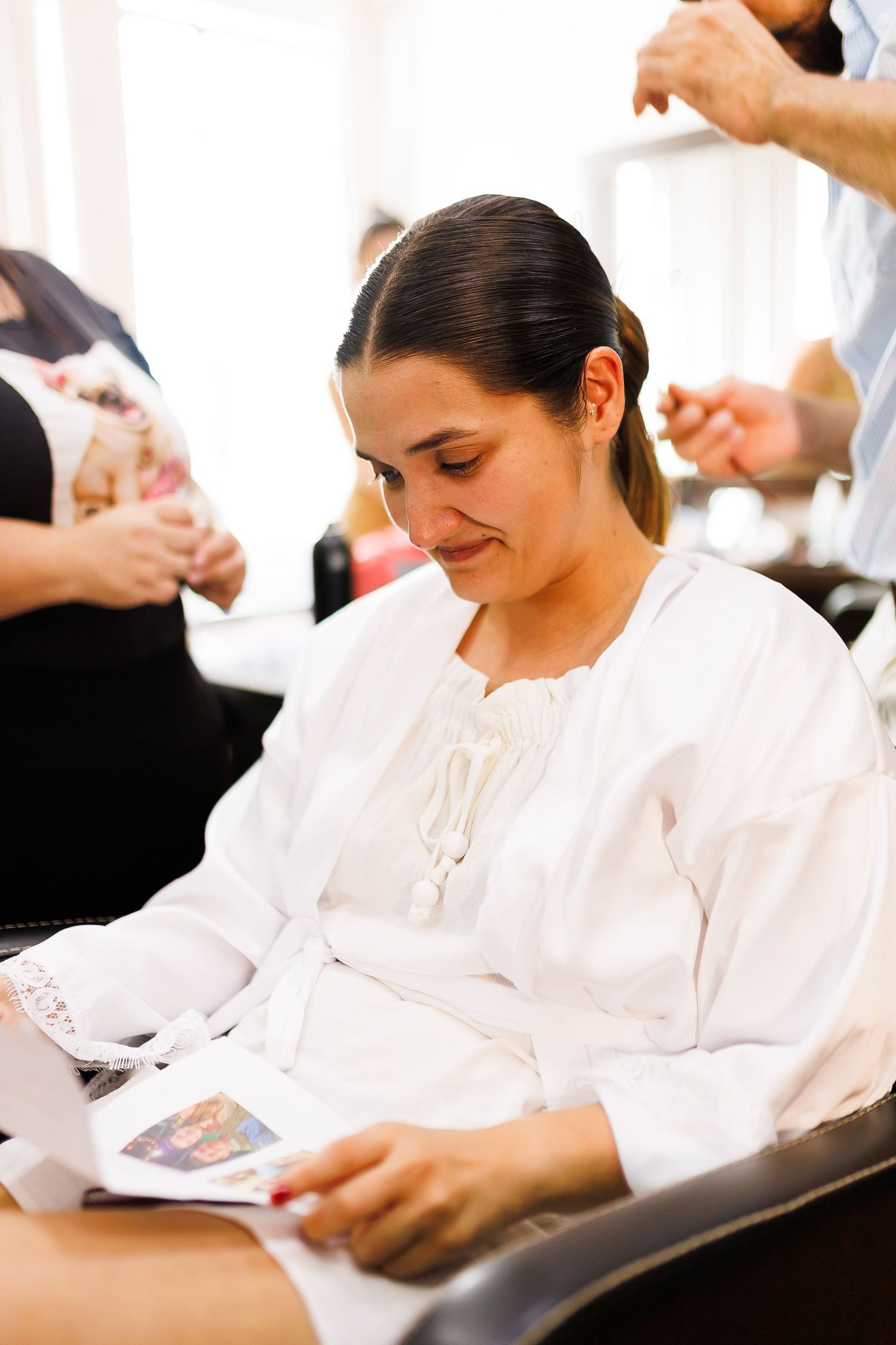 Woman in white blouse reading a magazine while sitting in a hair salon chair.