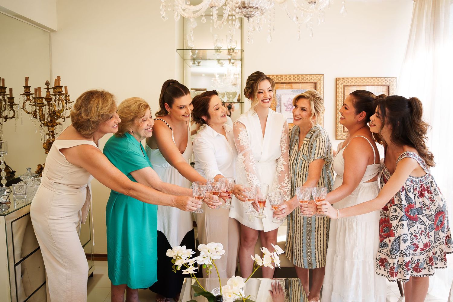 Bride and bridesmaids in elegant dresses toasting with champagne glasses during wedding preparations indoors.