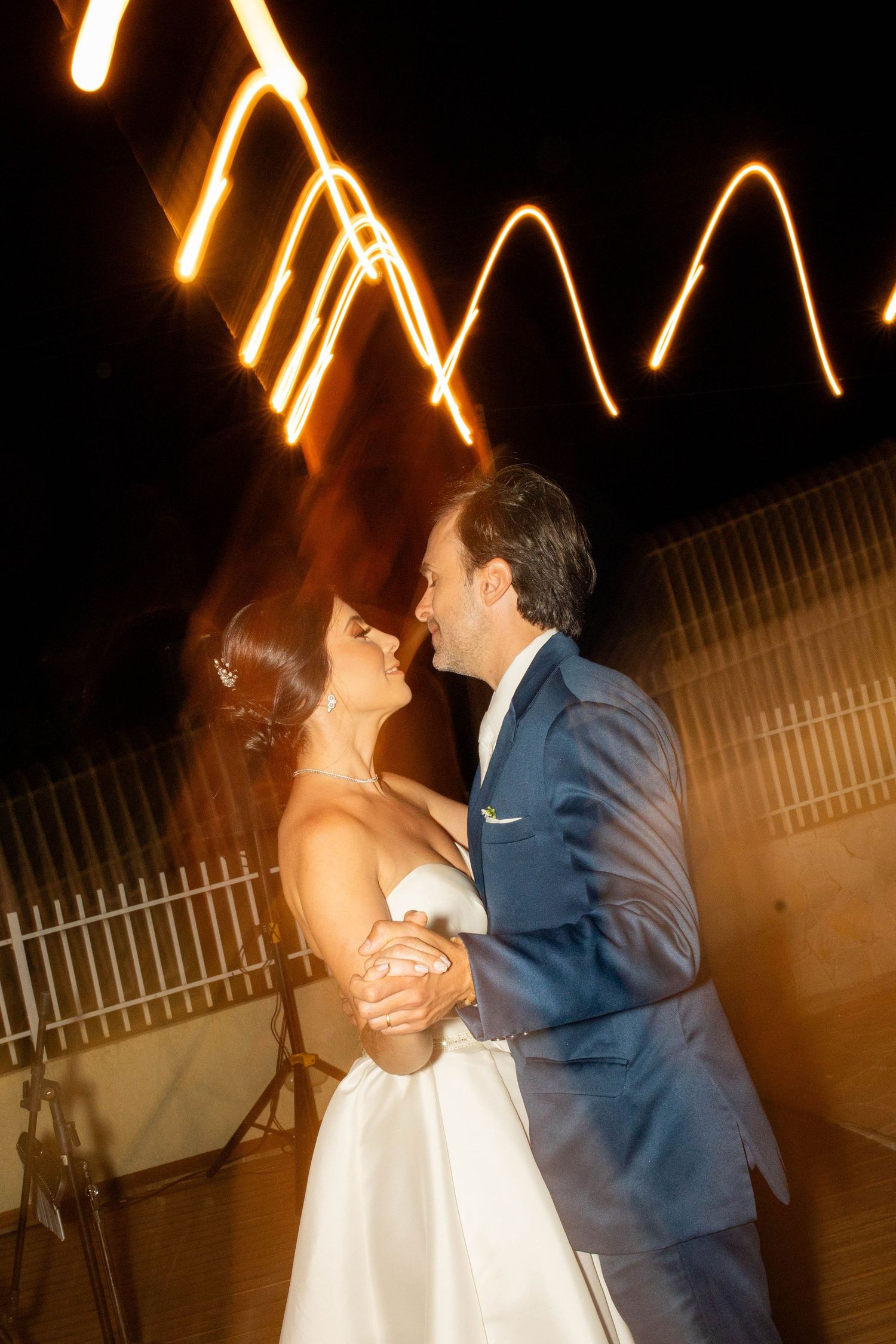 Bride and groom share their first dance outdoors at night with glowing light trails in the background.