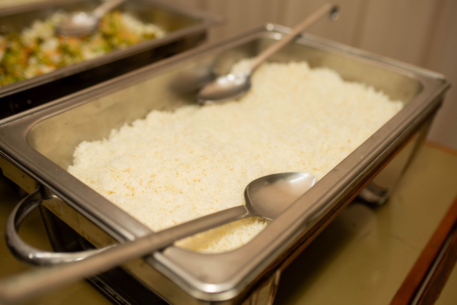 Buffet chafing dish filled with white rice and a serving spoon at a catered event.