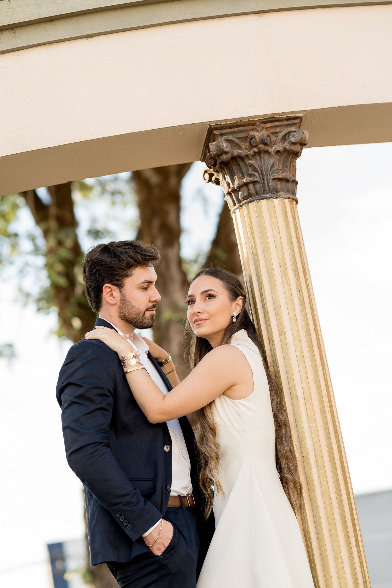 A bride and groom pose romantically beneath an elegant column at their outdoor wedding venue.