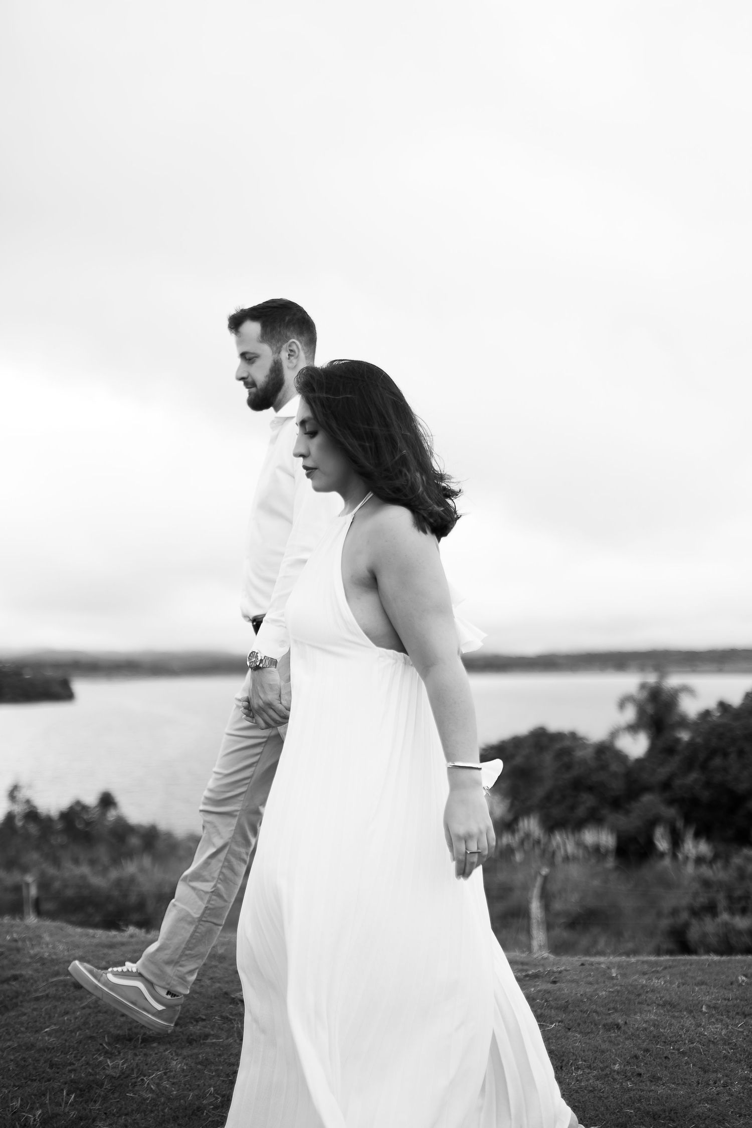 Black and white photo of a couple walking outdoors near a lake, woman in white dress, man in white shirt and khakis.