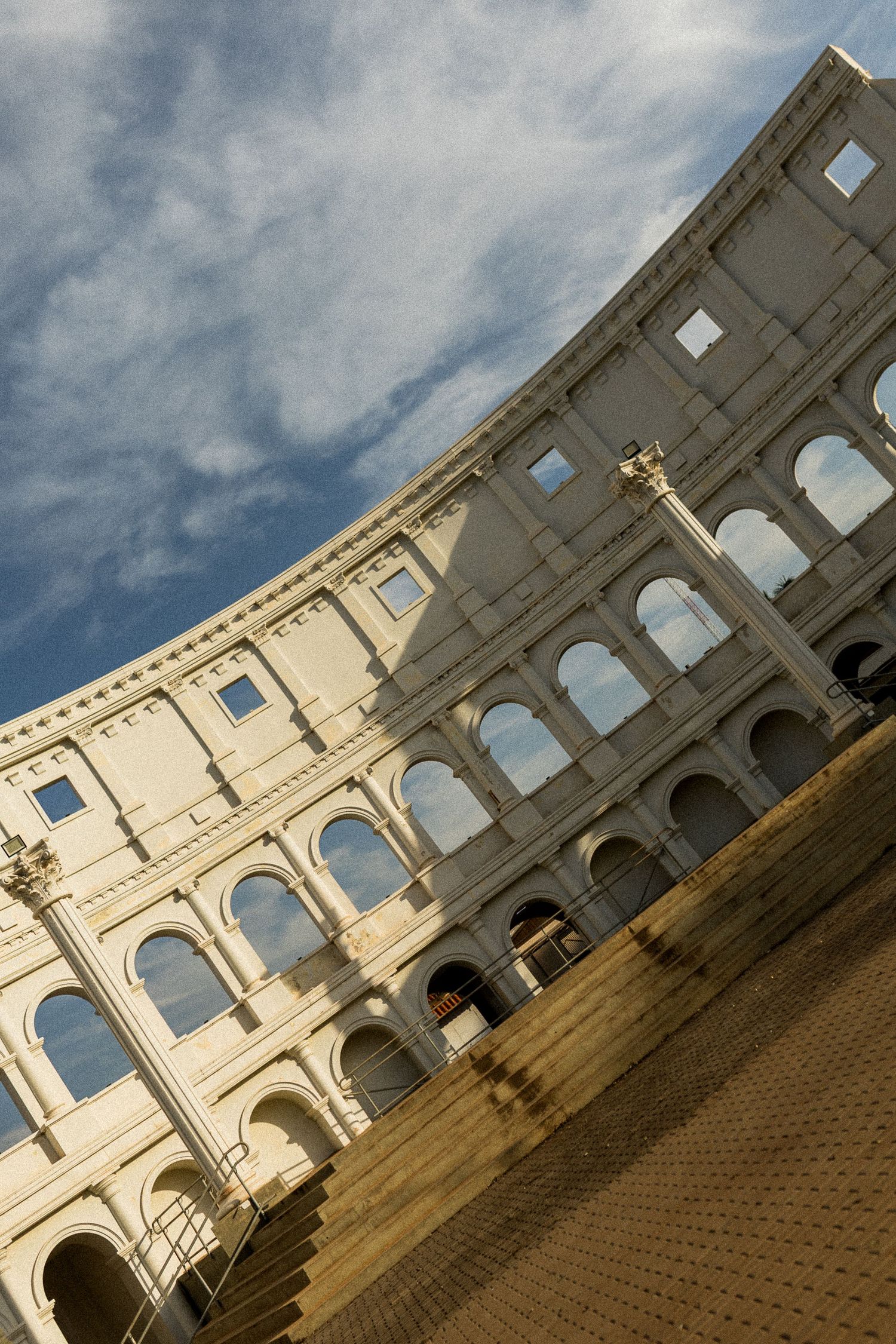 Dramatic low-angle view of the ancient Roman Colosseum exterior, showcasing its iconic arched facade against a partly cloudy sky.