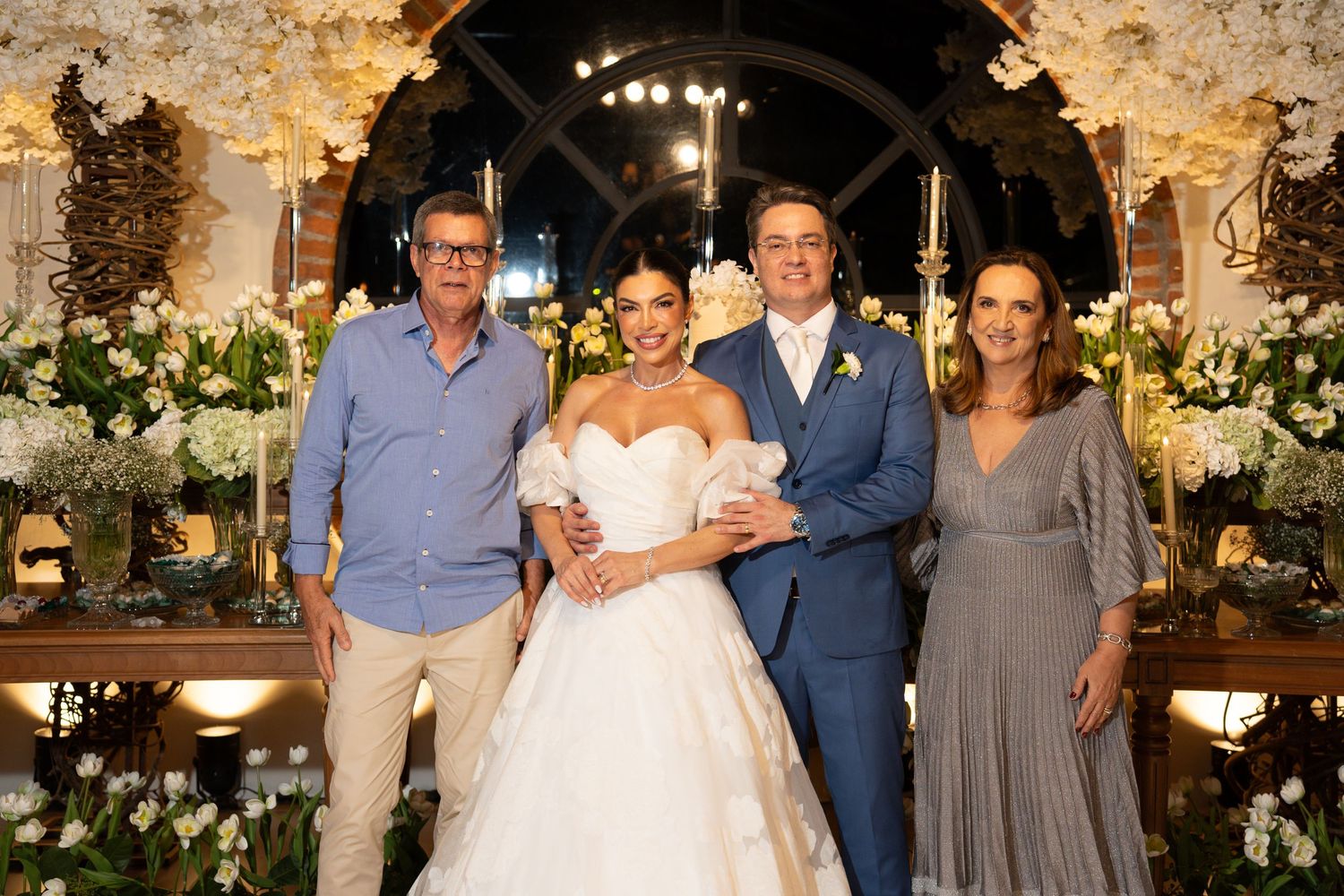 Bride in white gown and groom in suit pose with two guests at an elegant floral wedding ceremony.