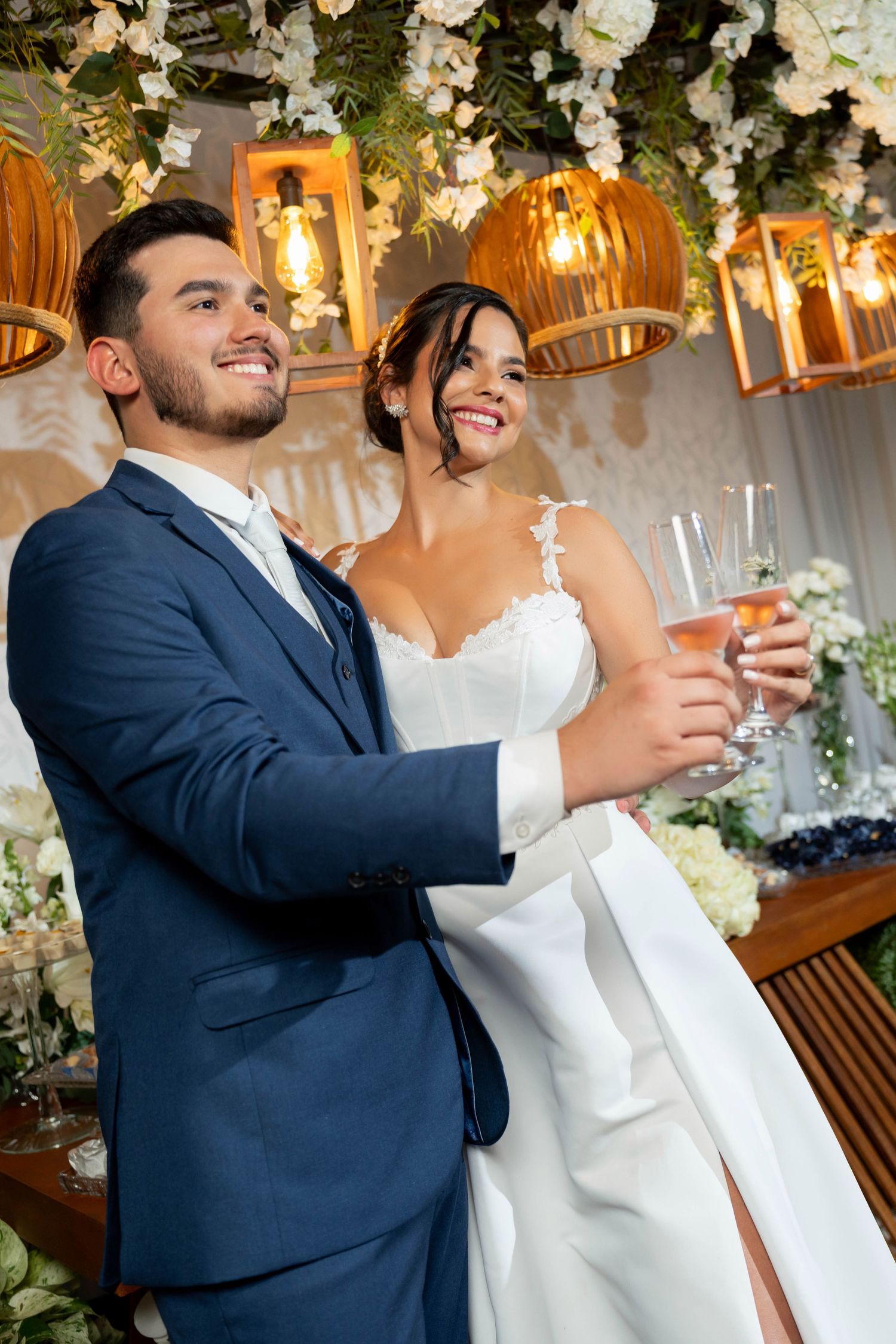 Smiling bride and groom toasting with champagne glasses at their elegant wedding reception with floral decorations.