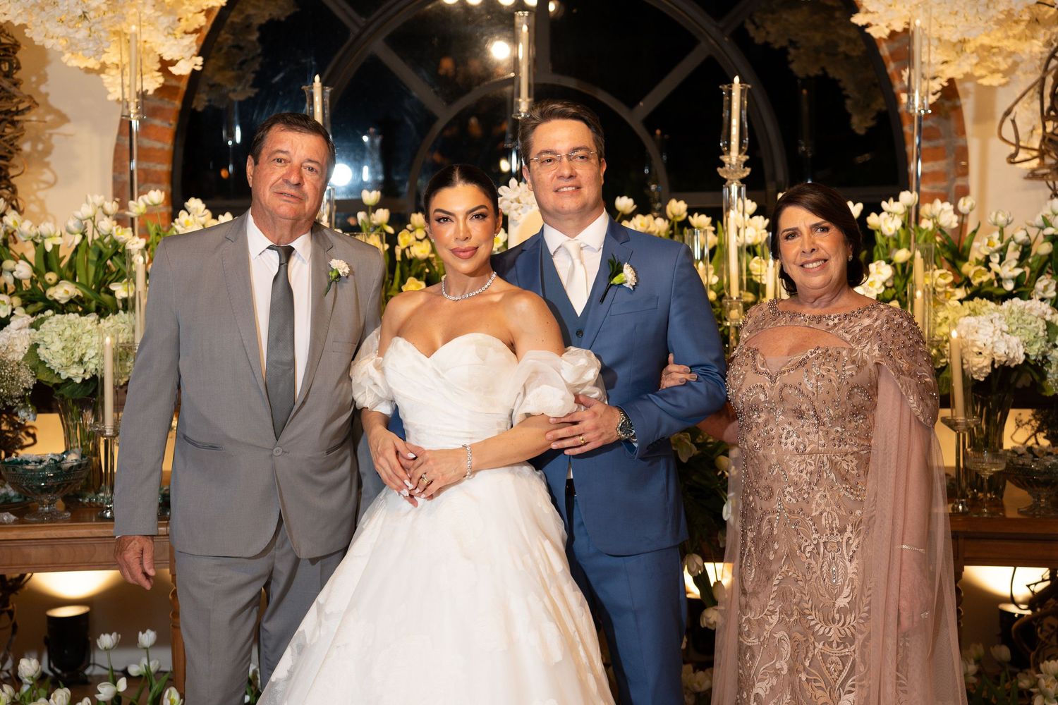 Bride and groom pose with family members in elegant wedding attire amid floral decorations.