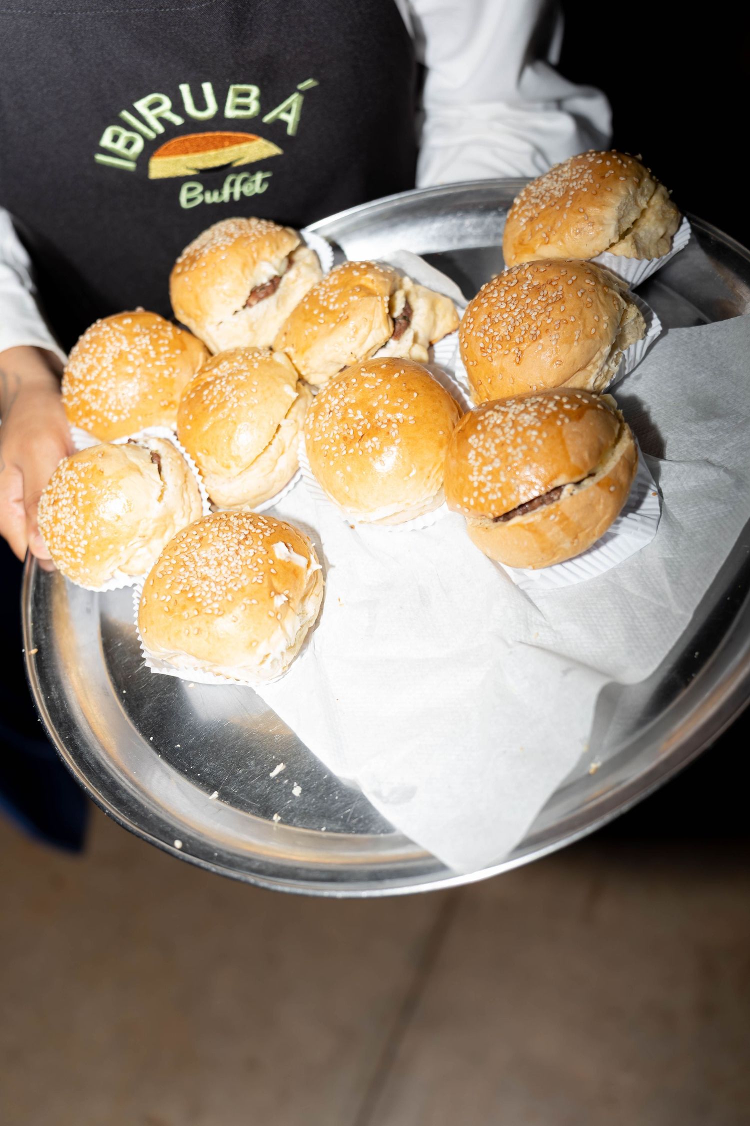 Server holding a silver tray of sesame seed slider buns at Ibiruba Buffet restaurant.
