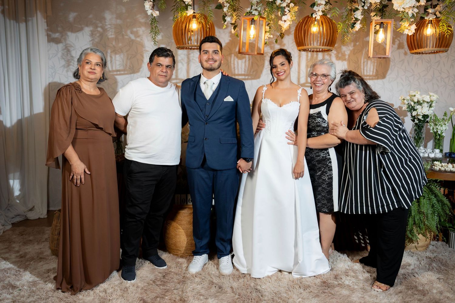 Bride and groom pose with four family members in elegant wedding venue with warm golden lighting and floral decor.