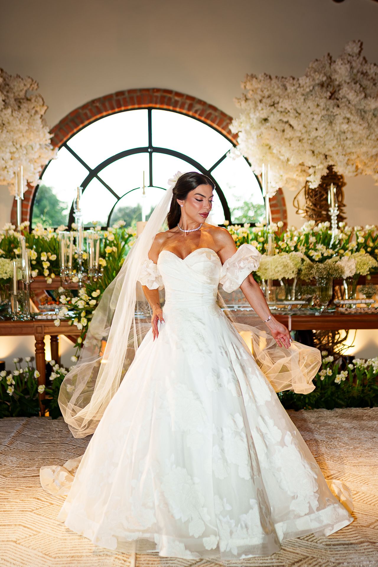 Bride in a white ball gown wedding dress with veil twirling in an elegant floral decorated reception venue.