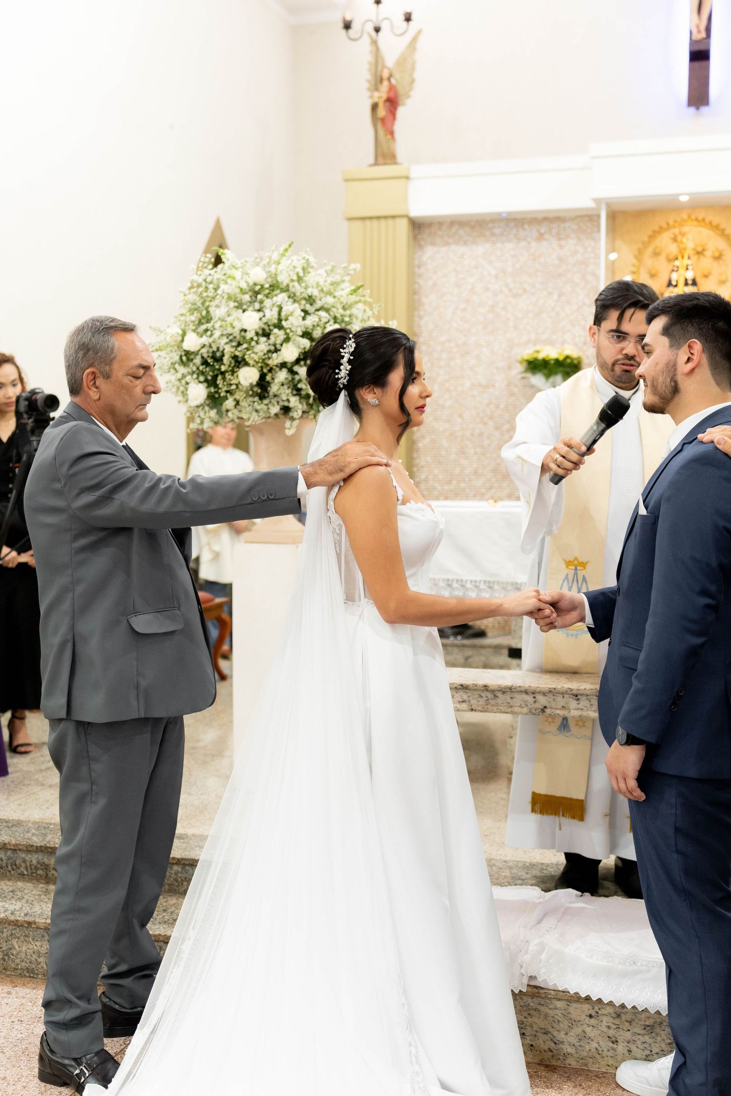 A bride and groom exchange vows at a church altar, with a priest and father of the bride present during the ceremony.