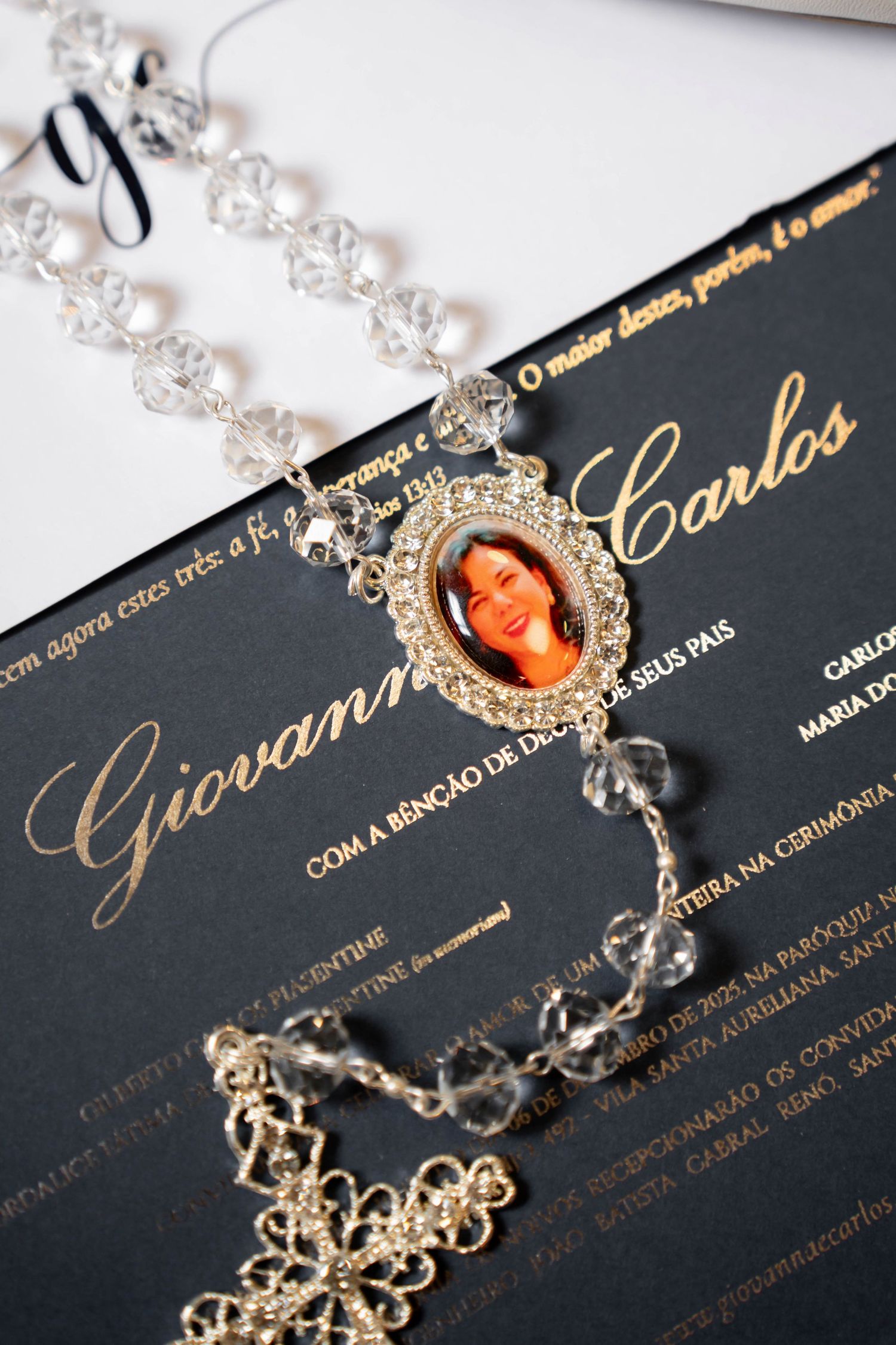 Black wedding invitation for Giovanna and Carlos with crystal rosary beads and oval photo charm pendant displayed elegantly.