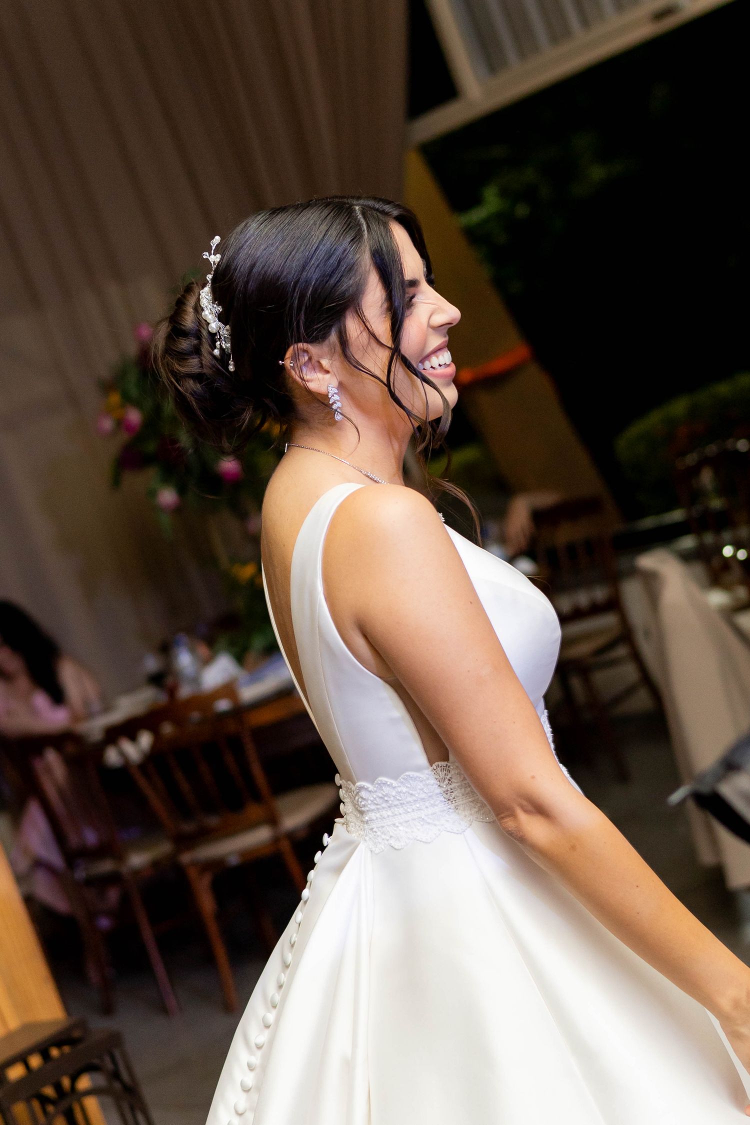 Smiling bride in a white satin wedding gown with floral hair accessories dancing at her wedding reception.