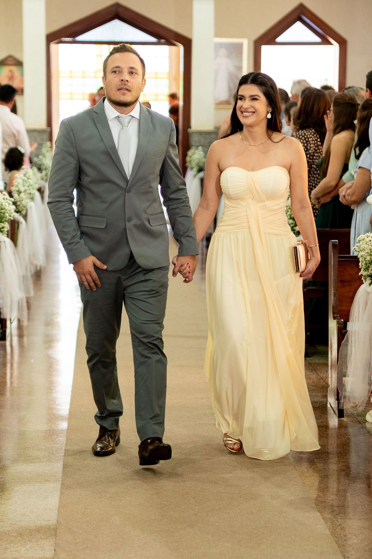 Couple walking down church aisle, man in gray suit, woman in strapless yellow gown, wedding ceremony.