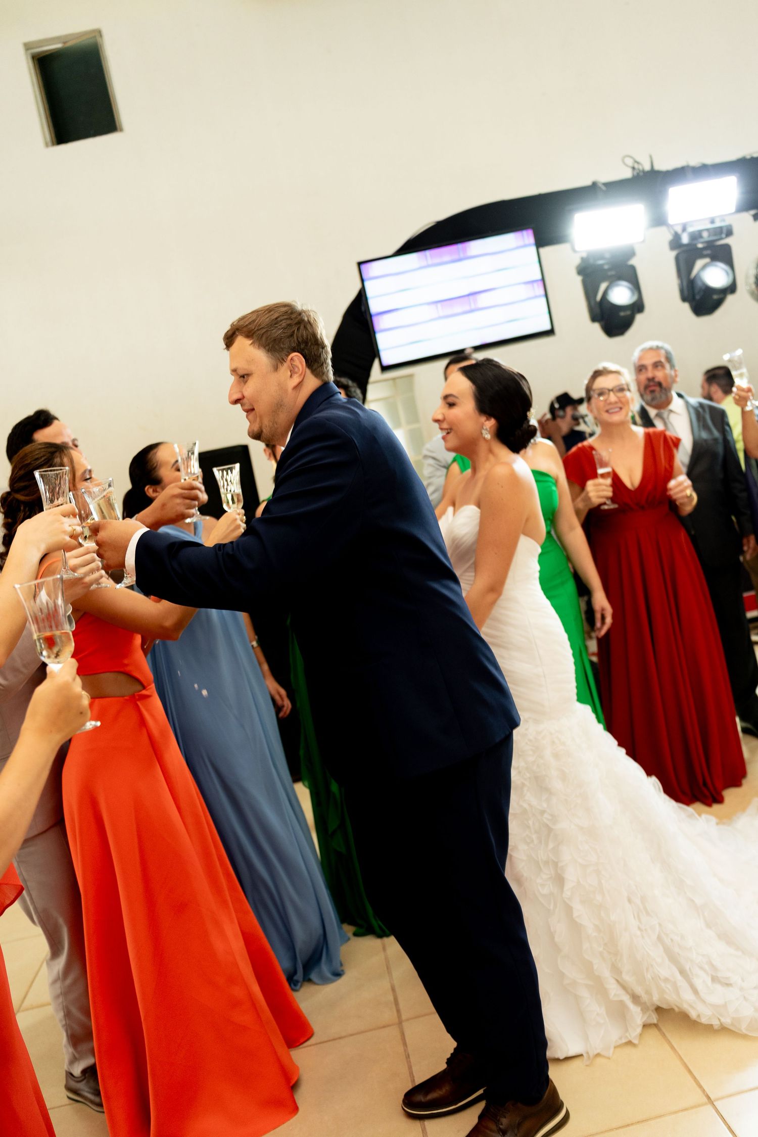 Bride and groom toasting champagne with guests in colorful gowns at a wedding reception celebration.