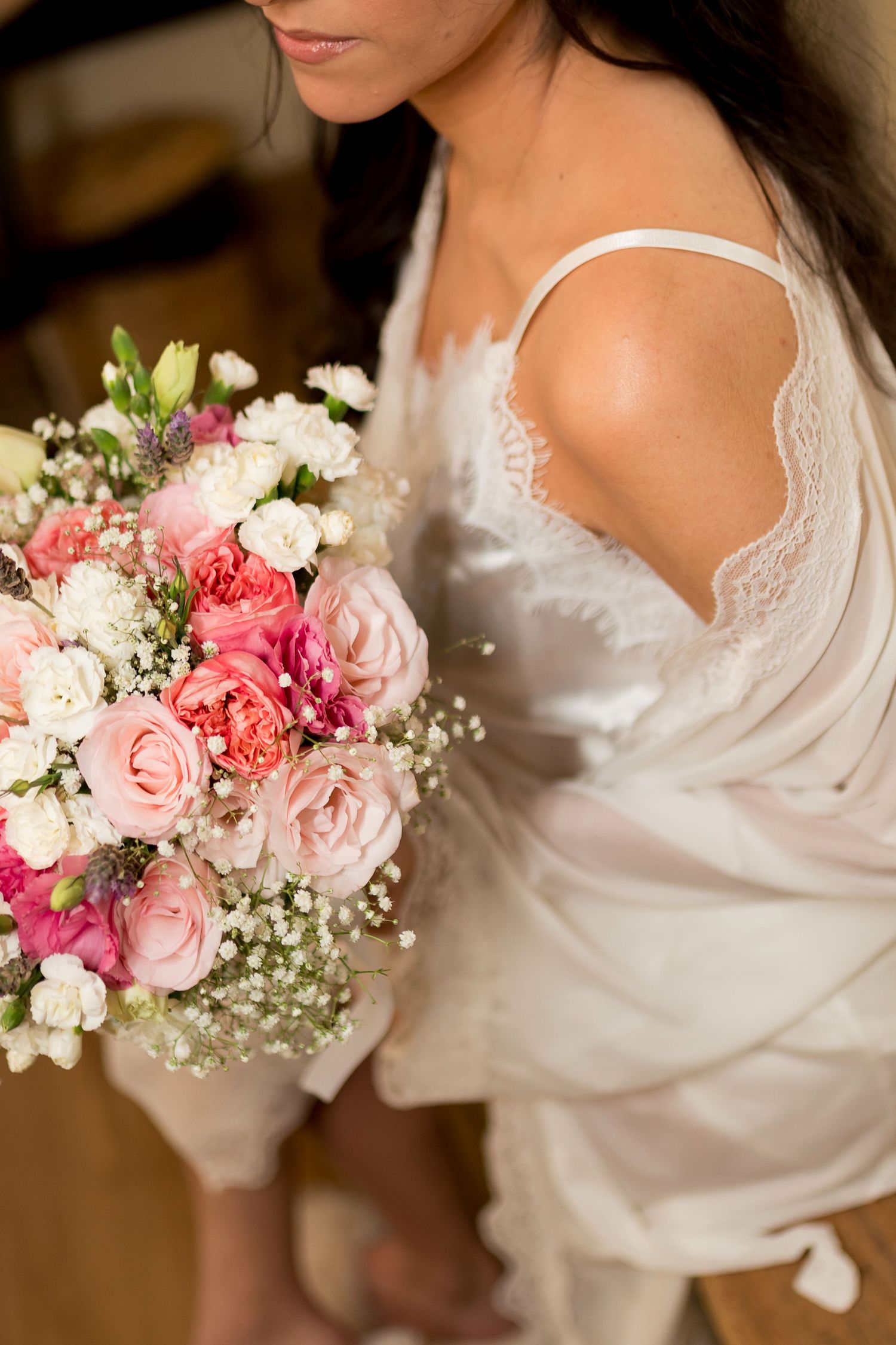 Bride in white lace lingerie holding a beautiful bouquet of pink roses and white flowers on her wedding day.