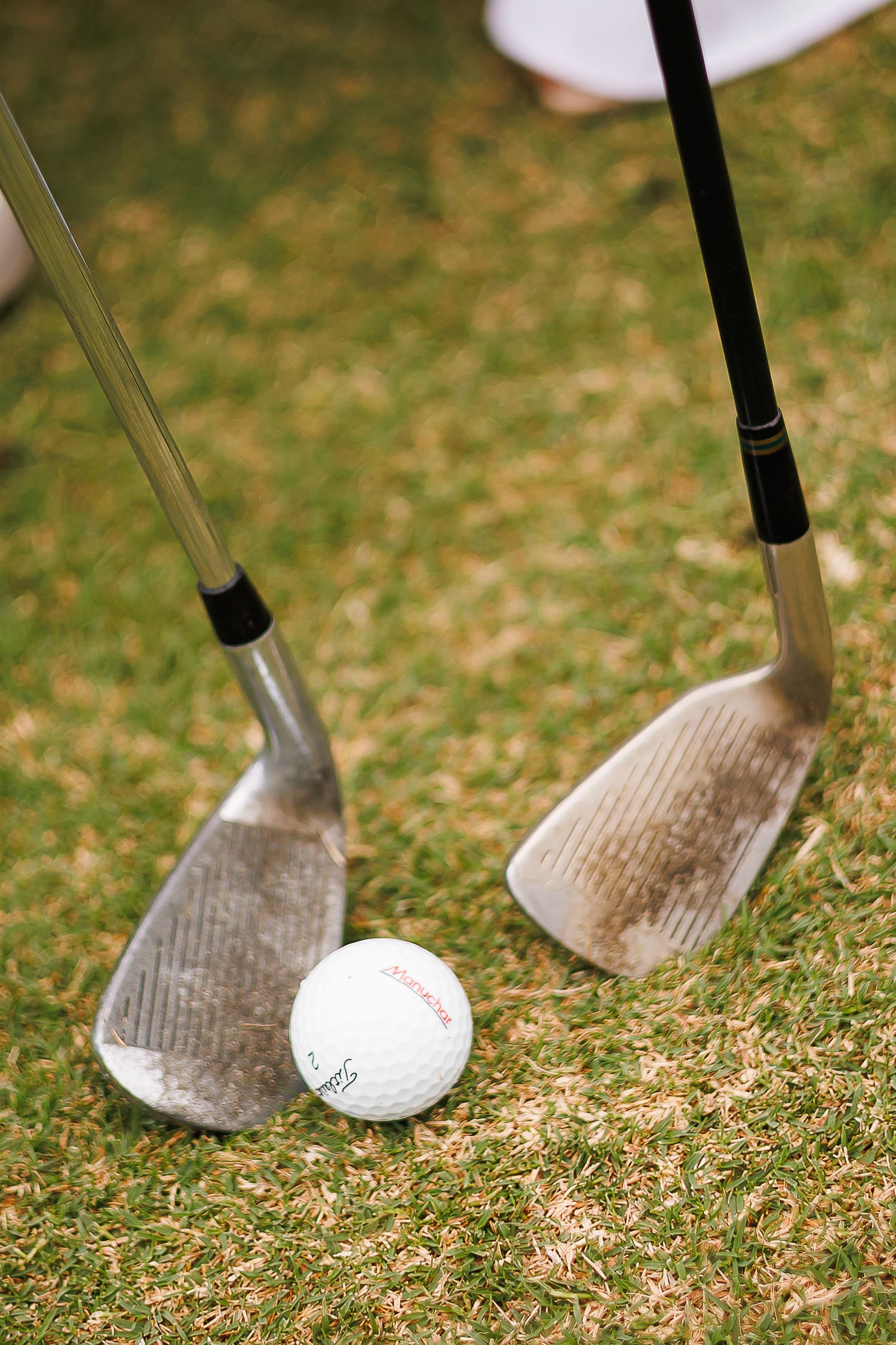 Two dirty golf clubs and a Titleist golf ball resting on green grass during a golf game.
