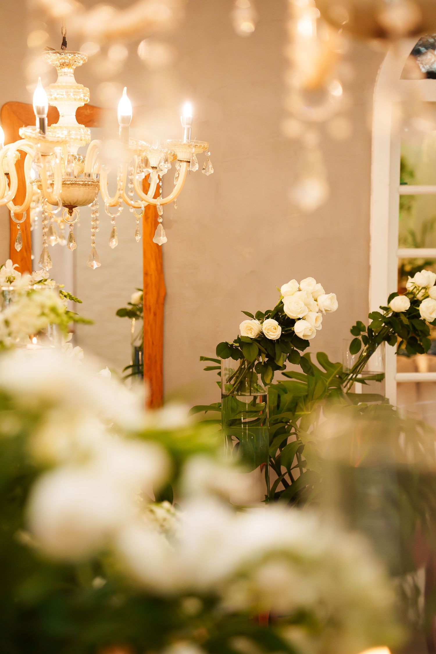 Elegant wedding venue with white roses in glass vases and a crystal chandelier glowing warmly in soft light.