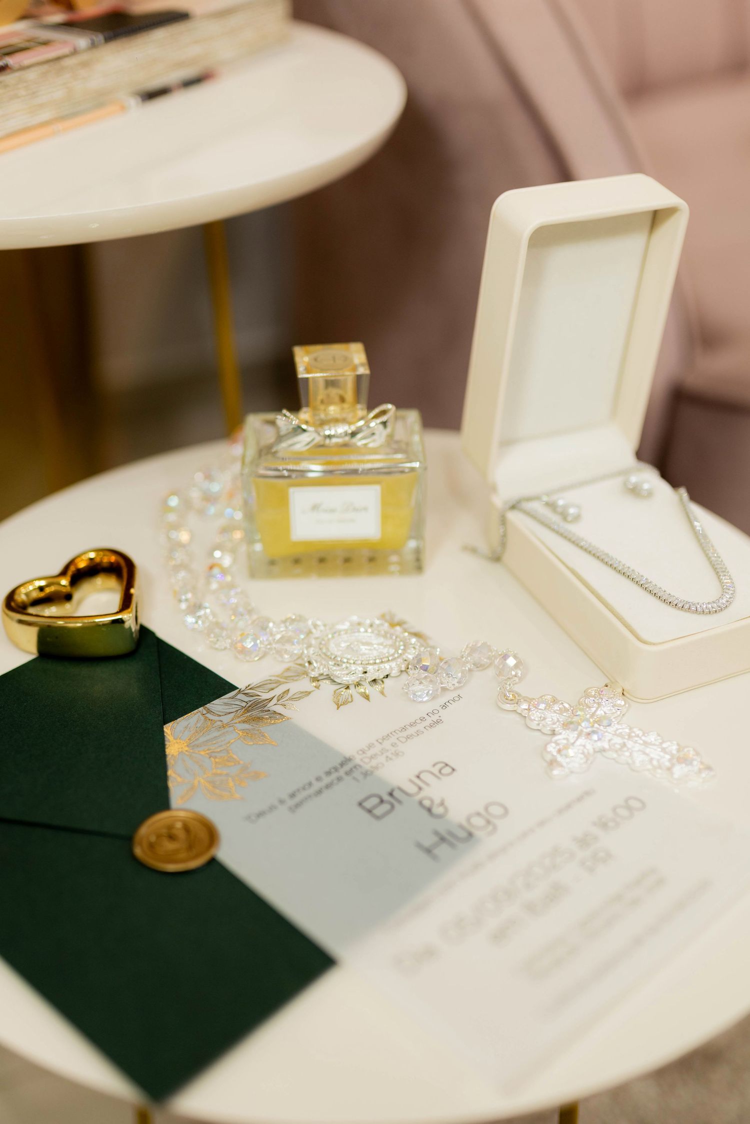 Elegant wedding flat lay with perfume bottle, diamond necklace in box, green envelope with wax seal, and floral invitation on marble table.