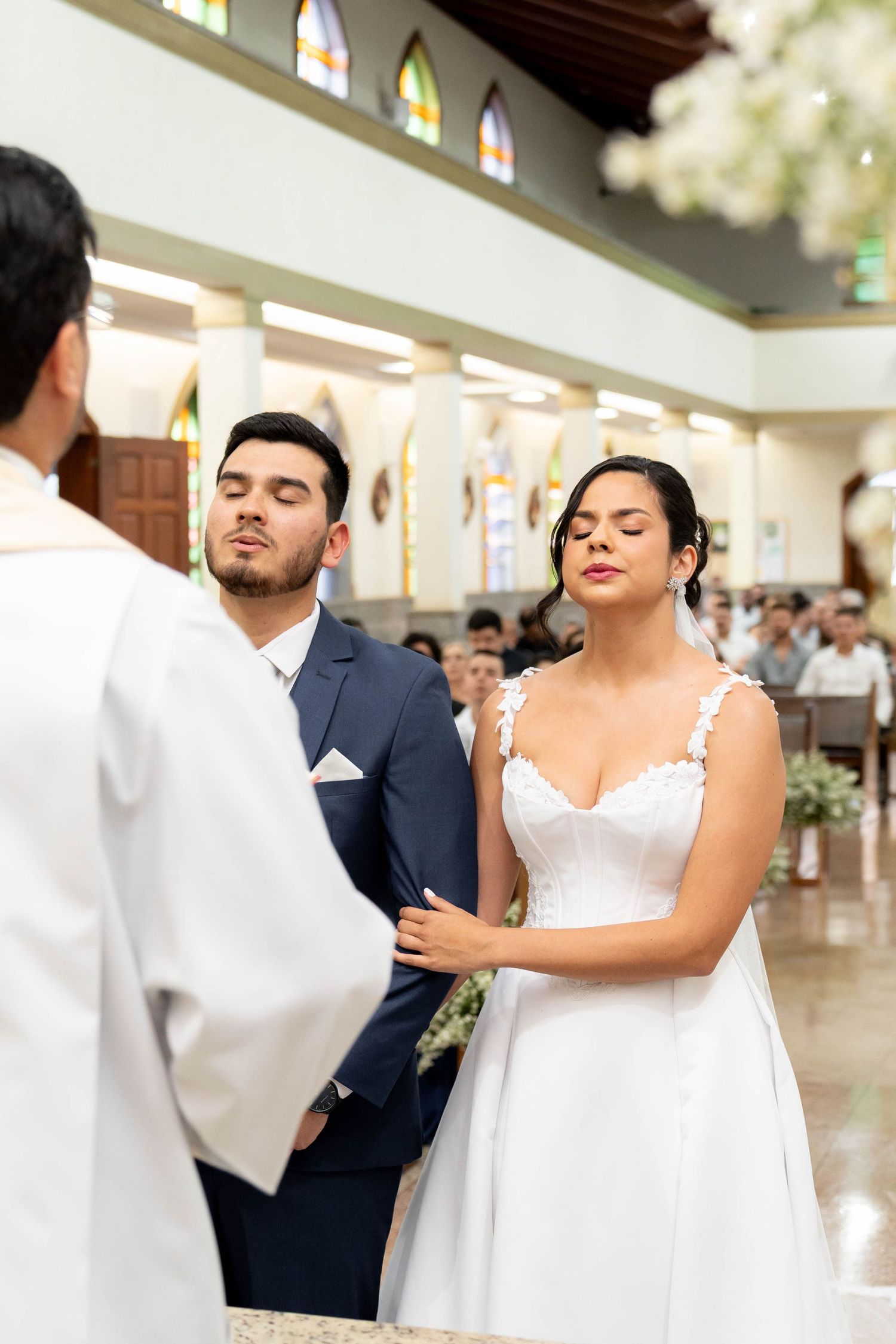 Bride and groom exchanging vows at church altar during wedding ceremony, bride in white lace dress, groom in blue suit.