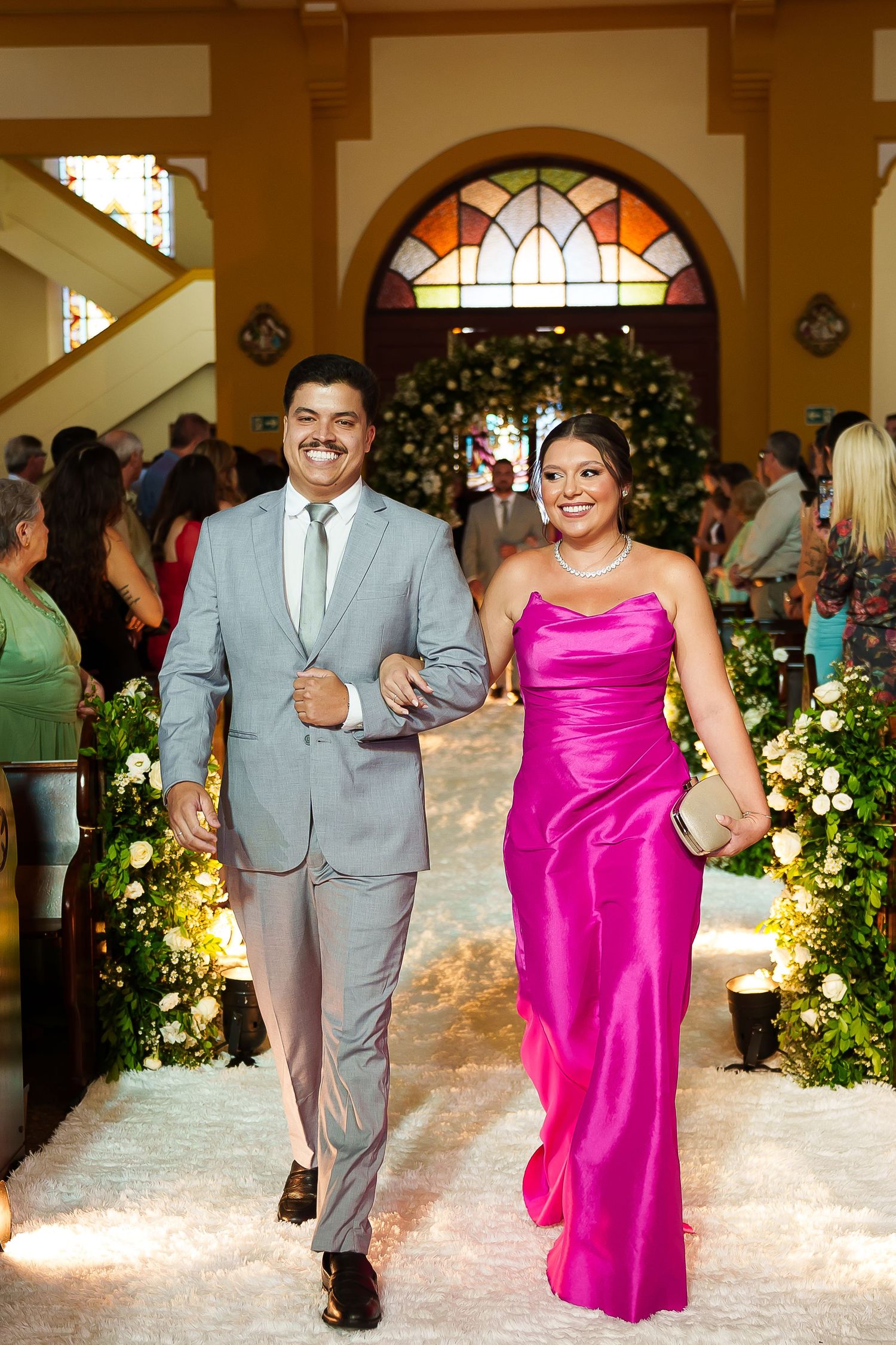 Couple walking down church aisle, man in gray suit, woman in pink satin gown, wedding ceremony.