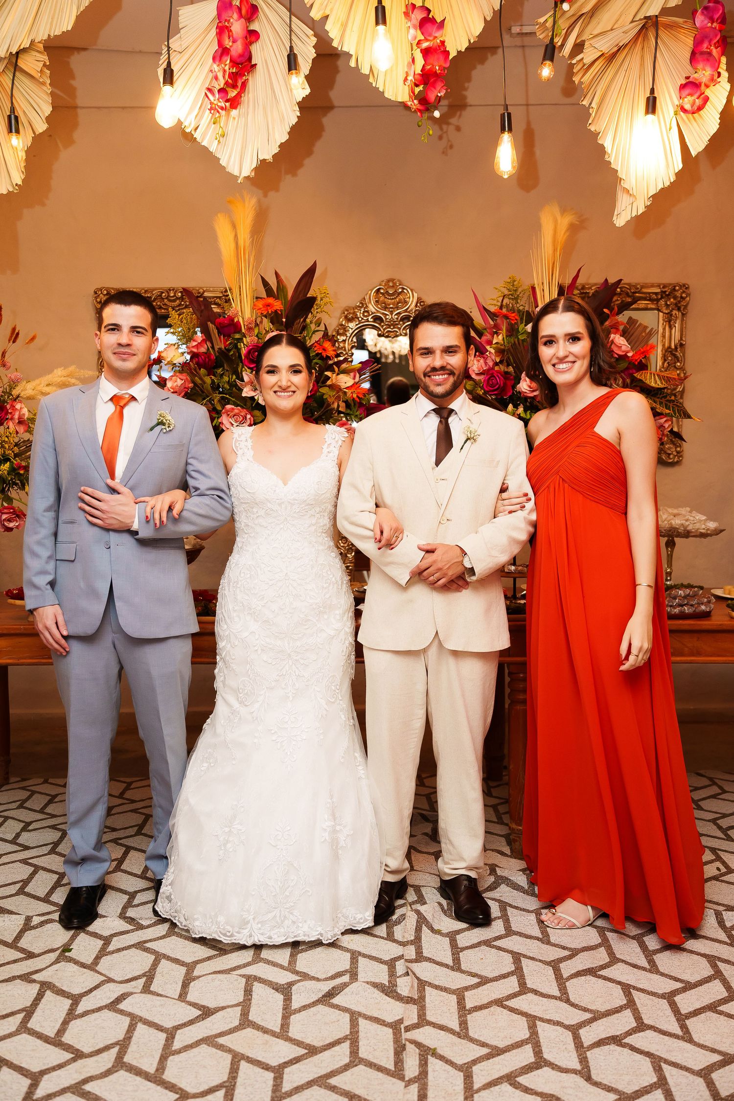 Wedding party posing elegantly, bride in white gown, groom in cream suit, groomsman in gray, bridesmaid in red dress.