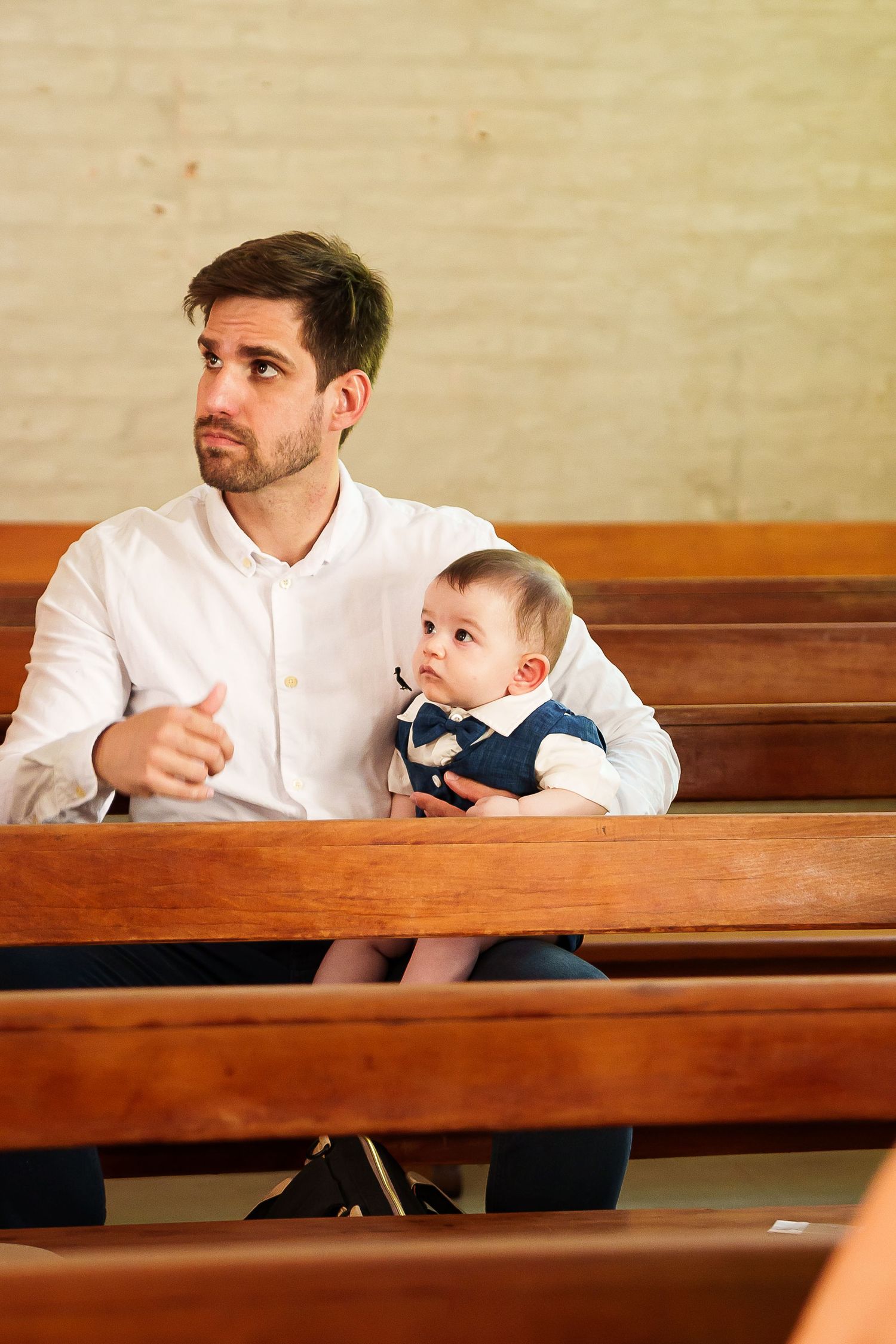 Father holding baby in church pew, both dressed smartly, man looking attentive during service.