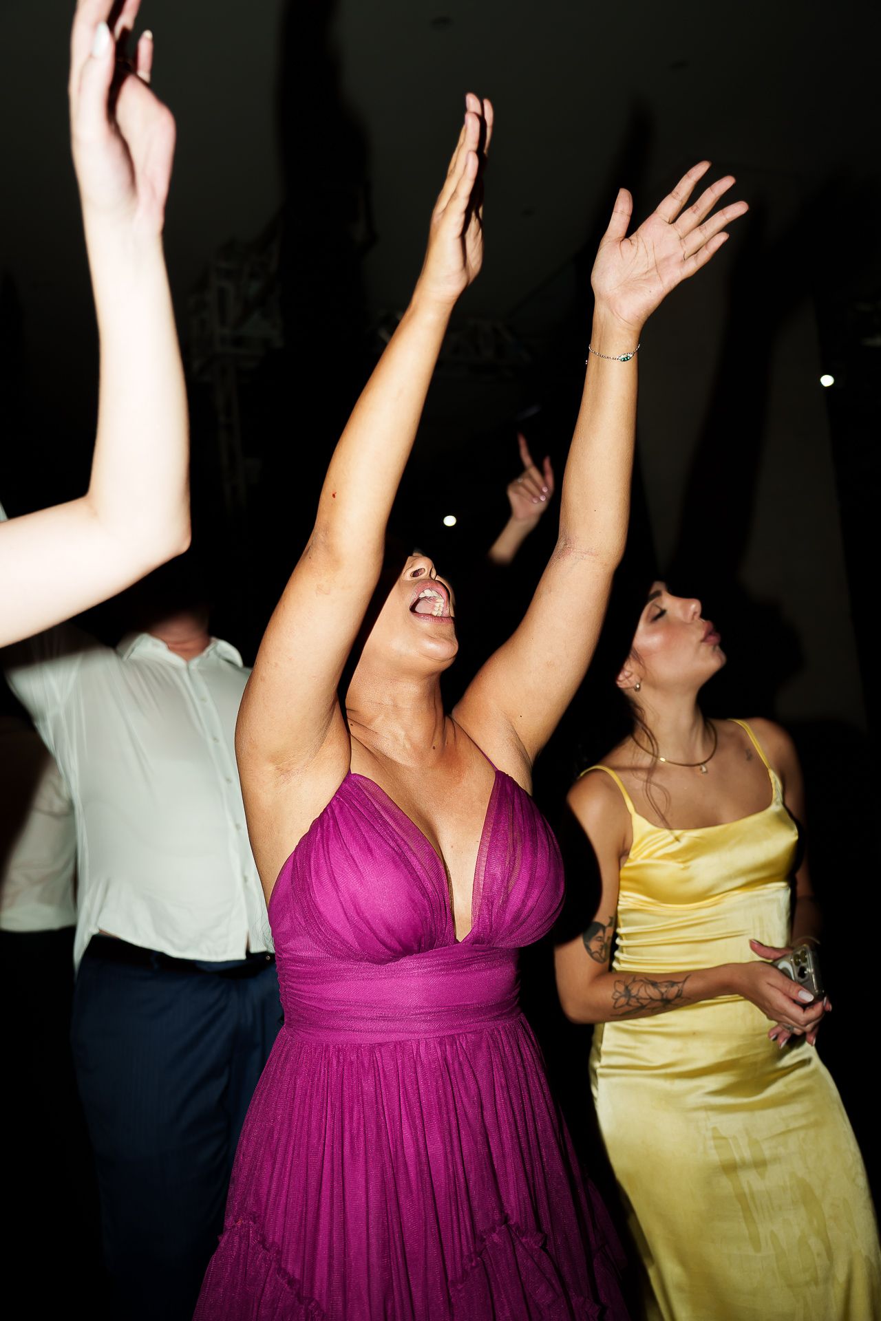 Women in colorful gowns dancing joyfully with arms raised at a formal evening event.