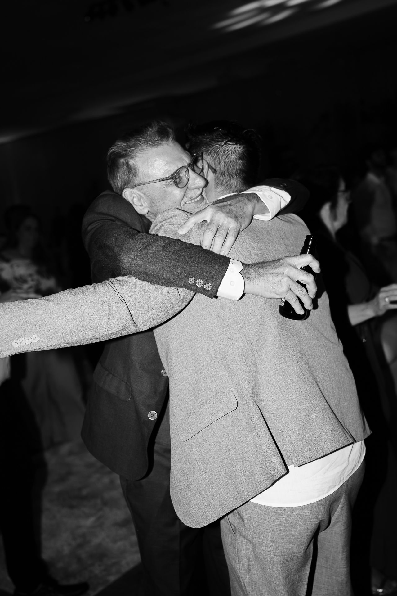 Two men in suits share a warm embrace at a formal event in this black and white photo.