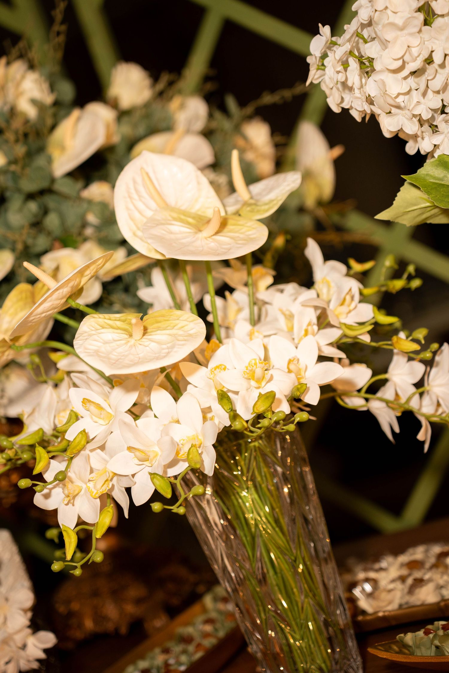 Elegant white anthurium and orchid floral arrangement in a glass vase with lush greenery.