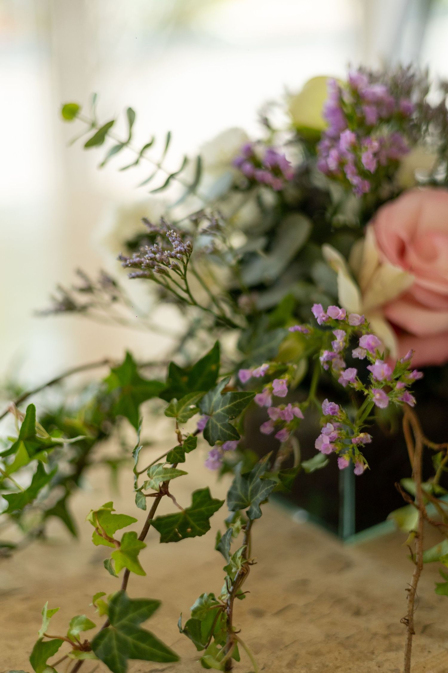 Close-up of a romantic floral arrangement with pink roses, lavender blooms, and trailing ivy greenery.