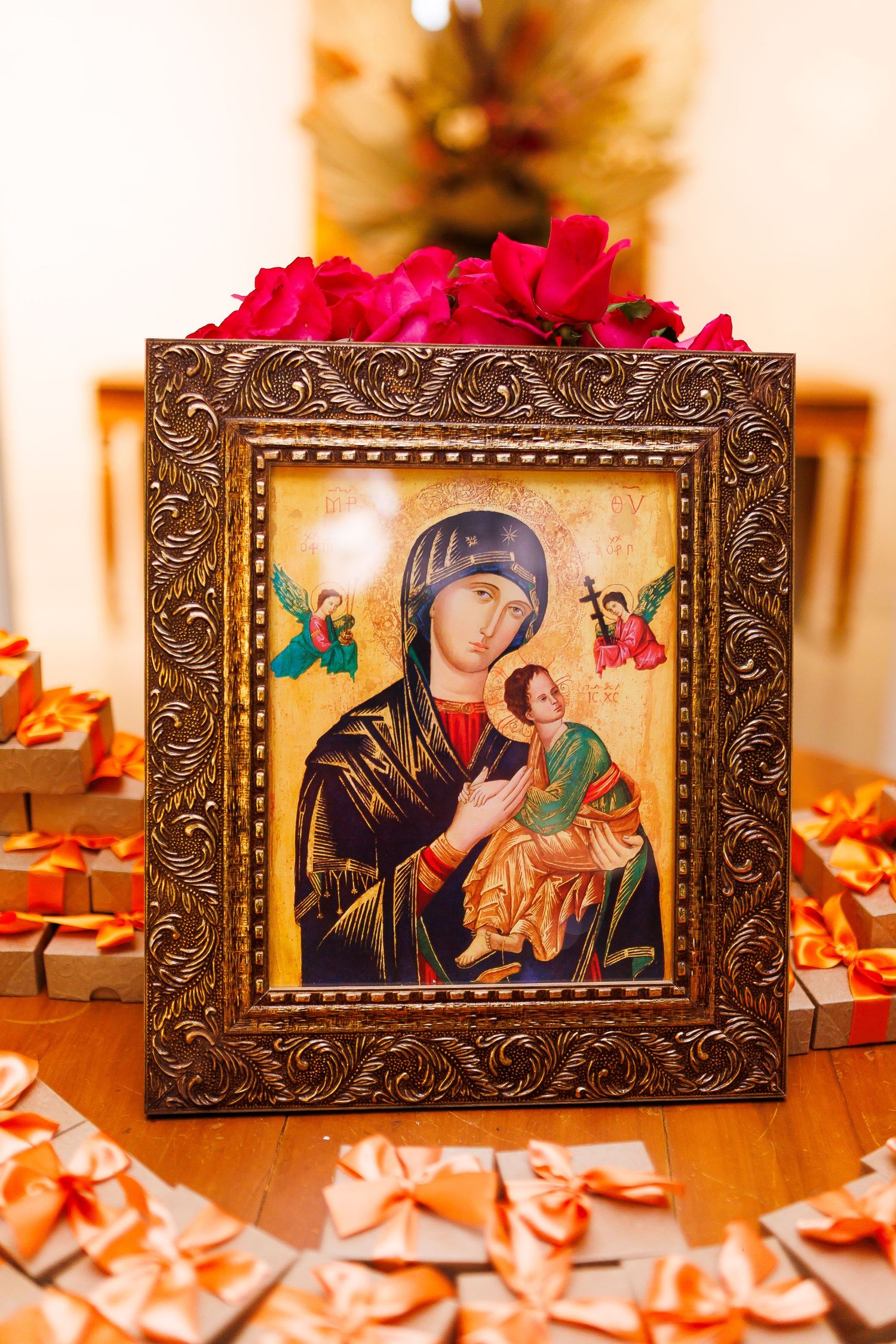 Ornate framed icon of Virgin Mary holding Baby Jesus surrounded by gift boxes with orange ribbons and red flowers.