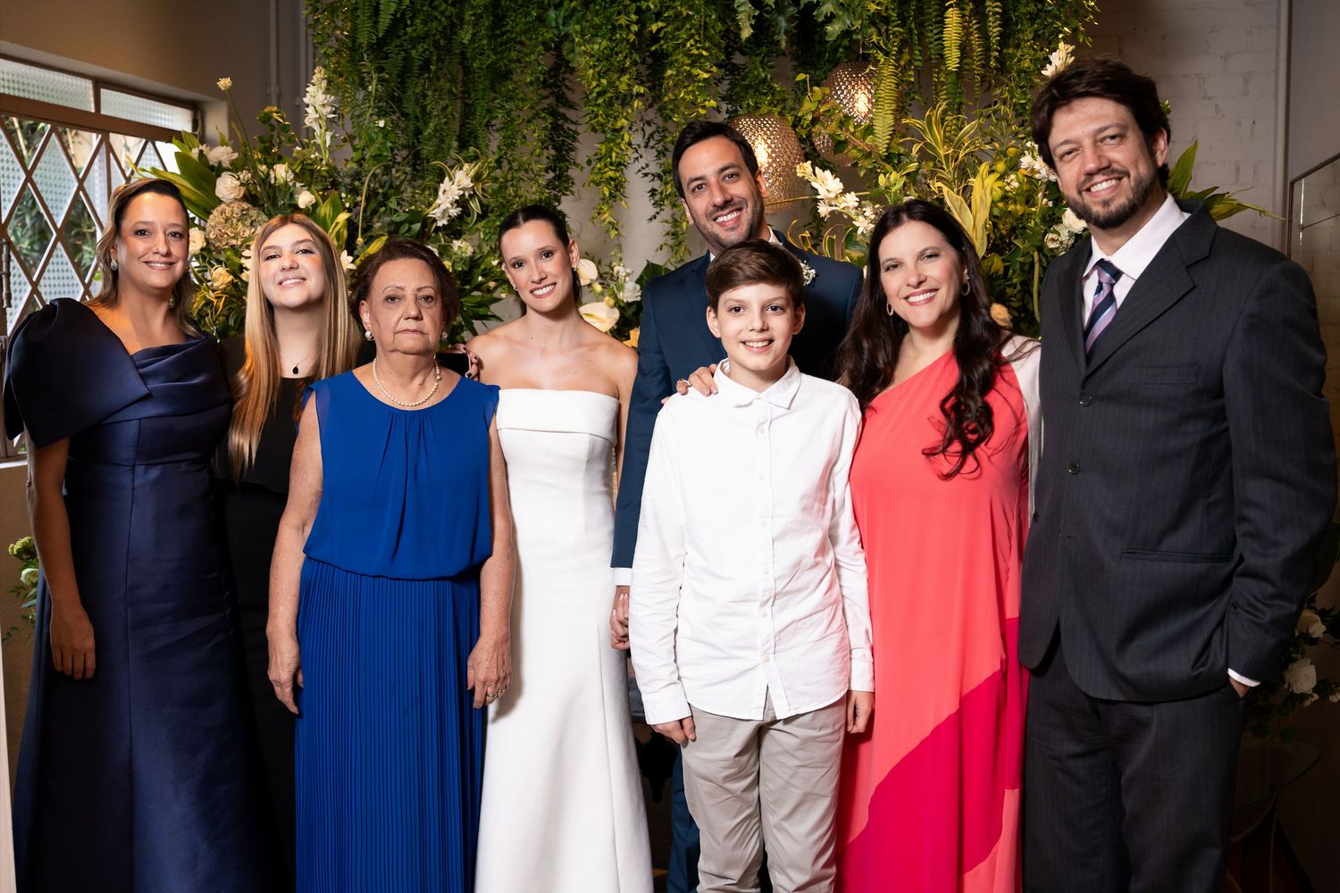 Wedding group photo with bride in white gown, groom, and family members posing together at elegant venue.