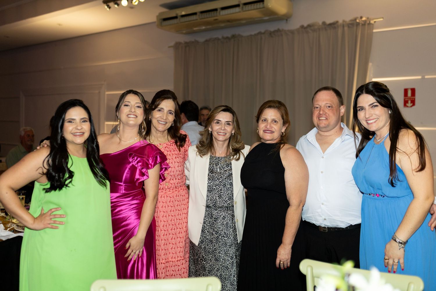 Group of seven elegantly dressed people posing together at a formal indoor event or celebration.