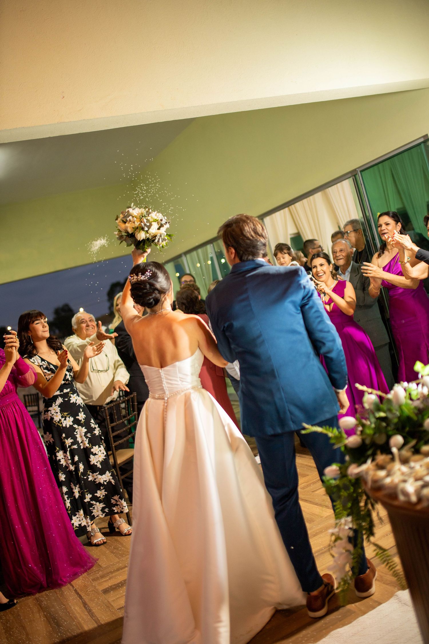 Bride tossing bouquet to guests in elegant white gown while groom in blue suit stands beside her at wedding reception.