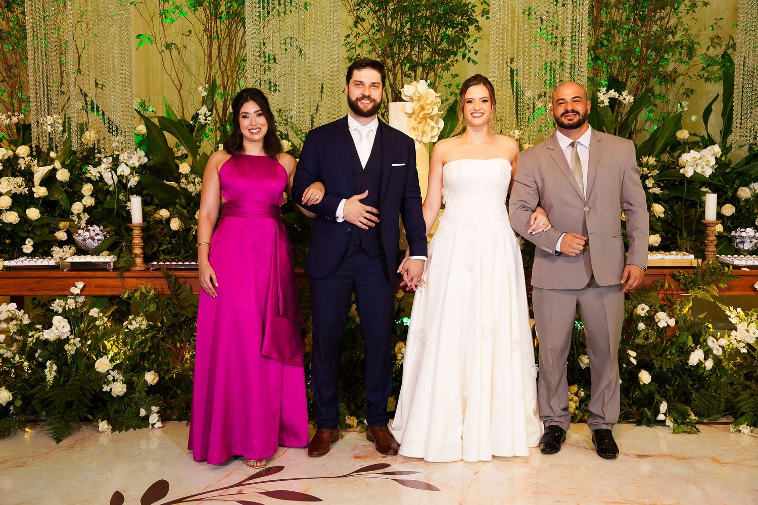 Wedding party of four posing elegantly in a floral decorated venue, bride in white gown, guests in formal attire.
