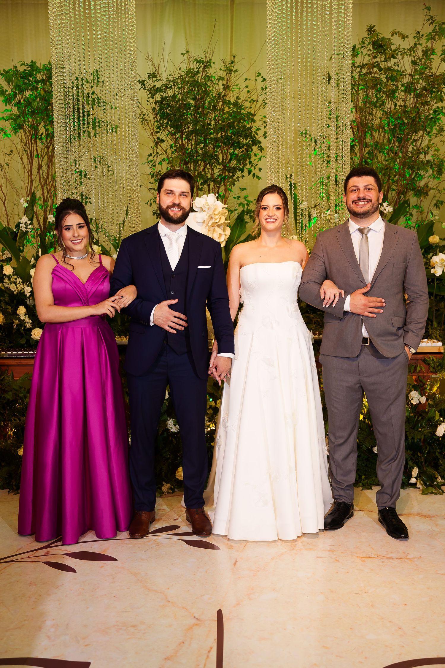 Wedding party posing elegantly, bride in white gown, groom in navy suit, guests in magenta dress and gray suit.