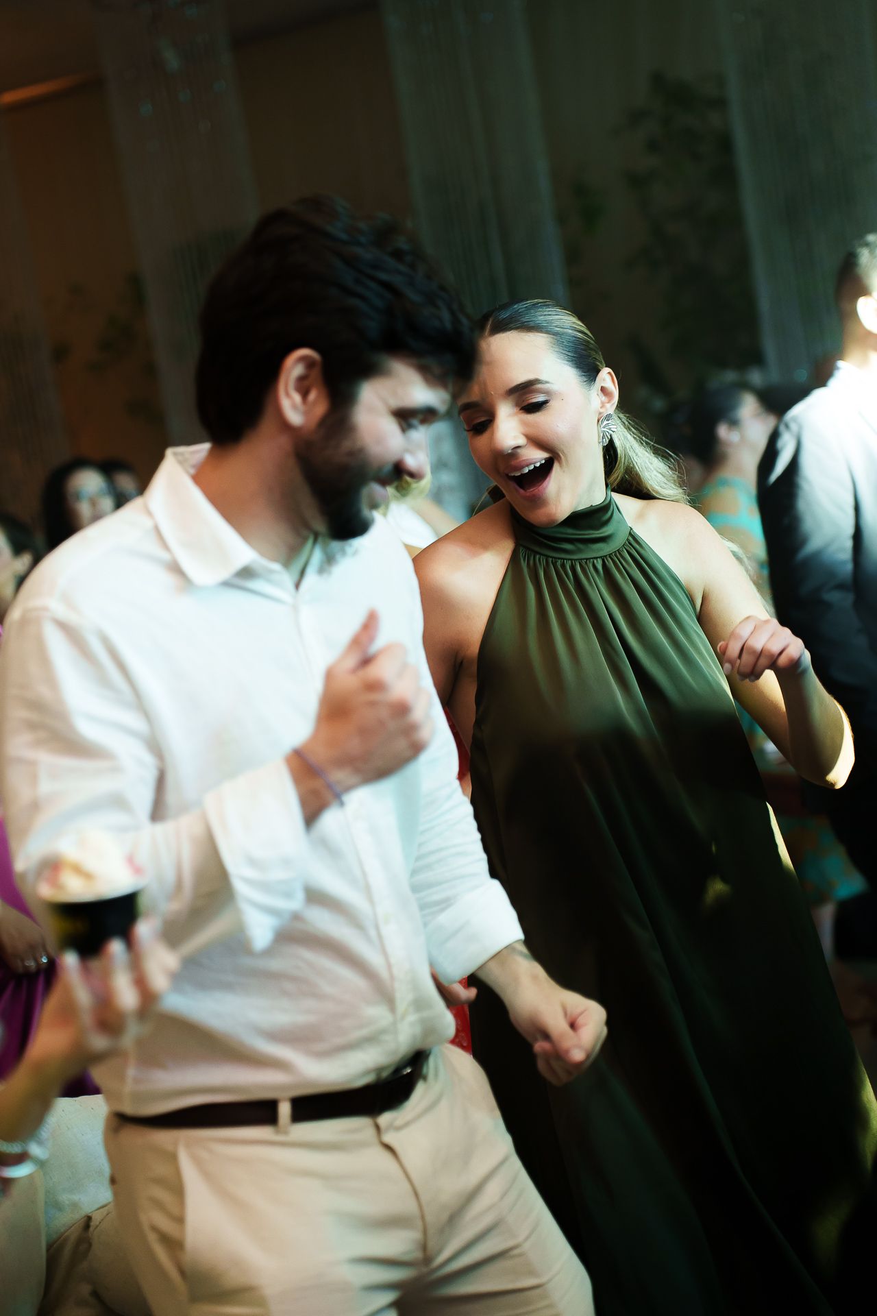 A couple in elegant attire dancing joyfully at a formal event, woman in green halter dress laughing.