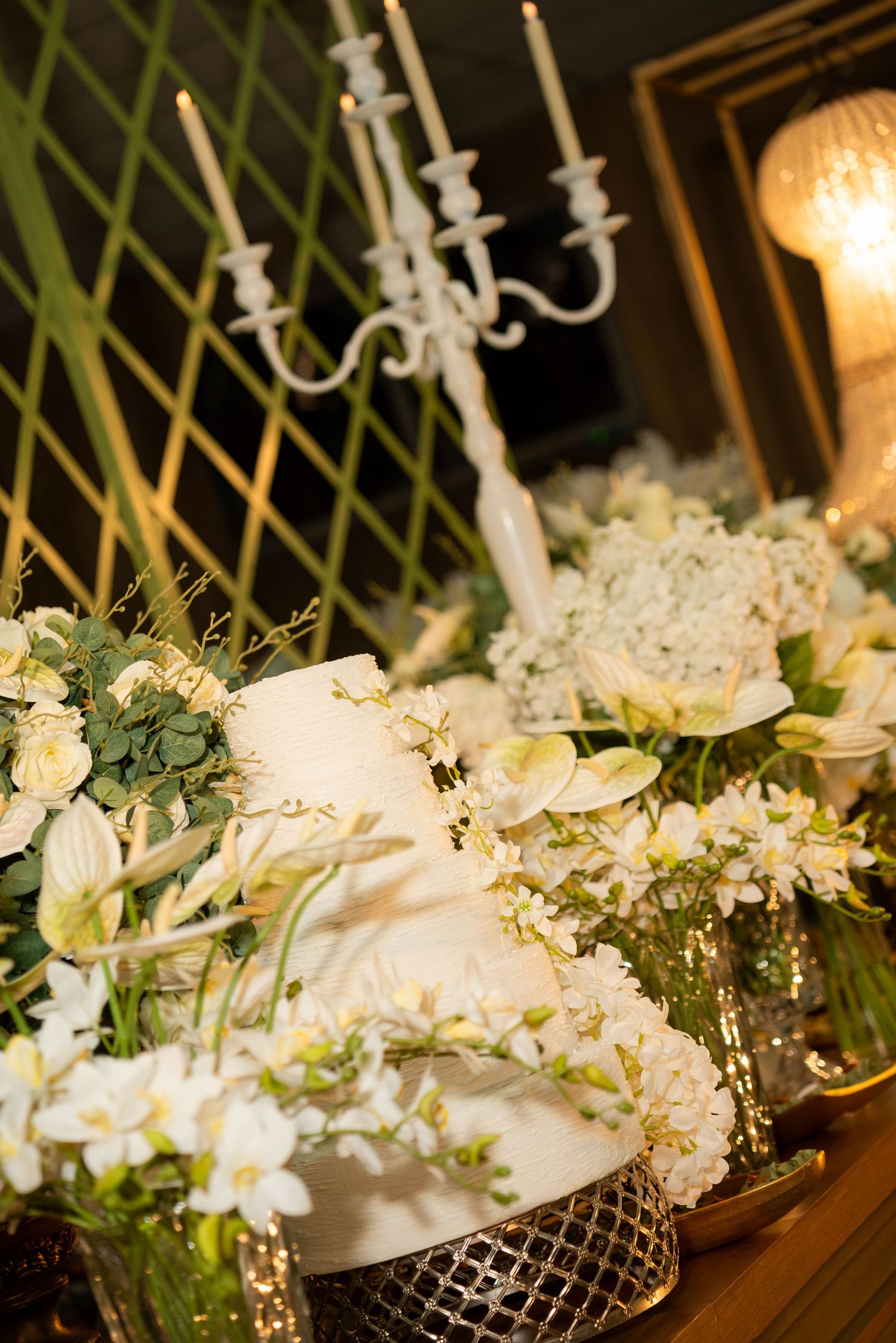 Elegant wedding cake surrounded by white floral arrangements and a candelabra centerpiece on a decorated table.
