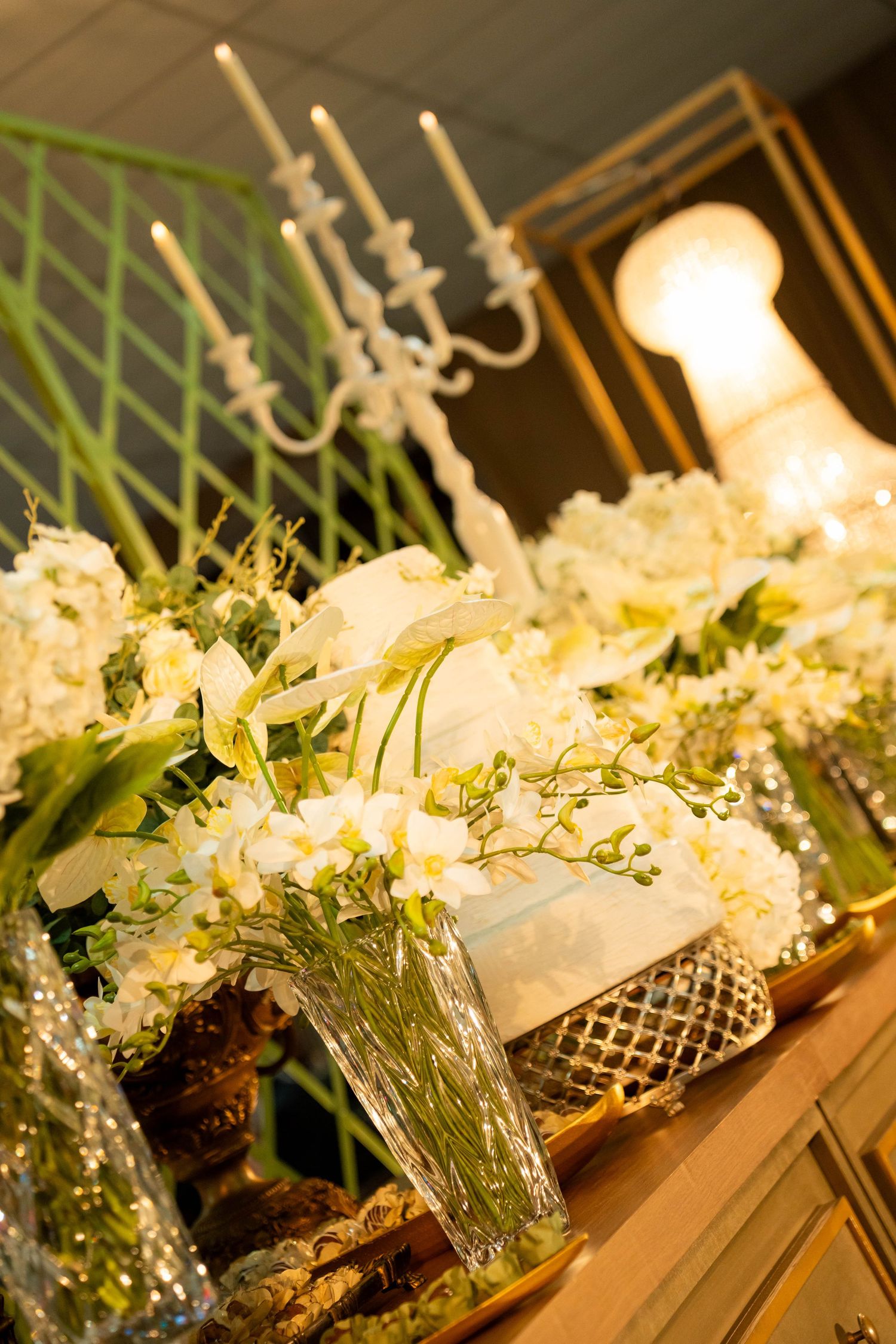 Elegant white floral arrangements with hydrangeas and orchids displayed on a gold table with candelabra at a wedding reception.