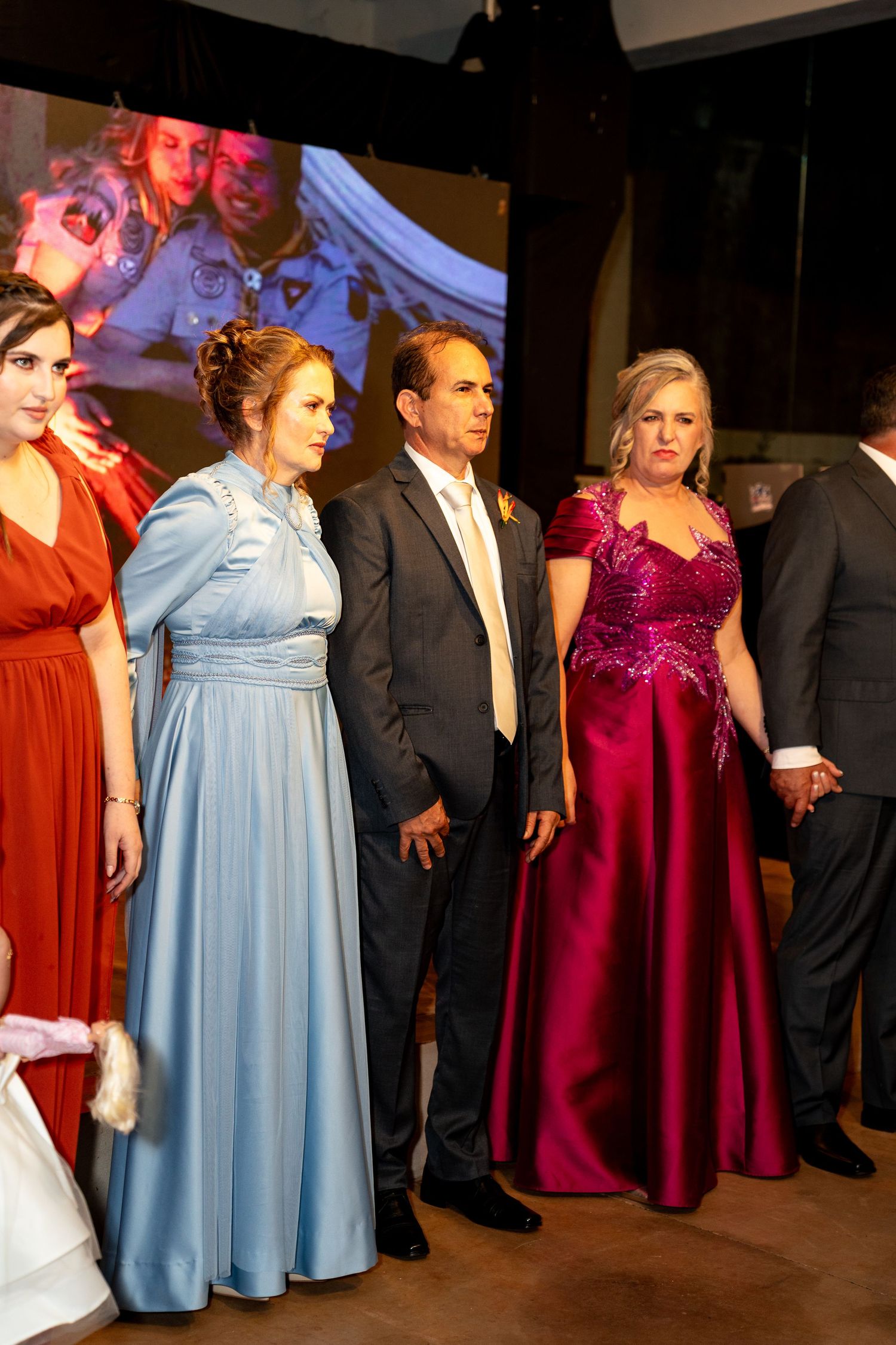 Group of elegantly dressed people in formal gowns and suits posing at a sophisticated evening event.