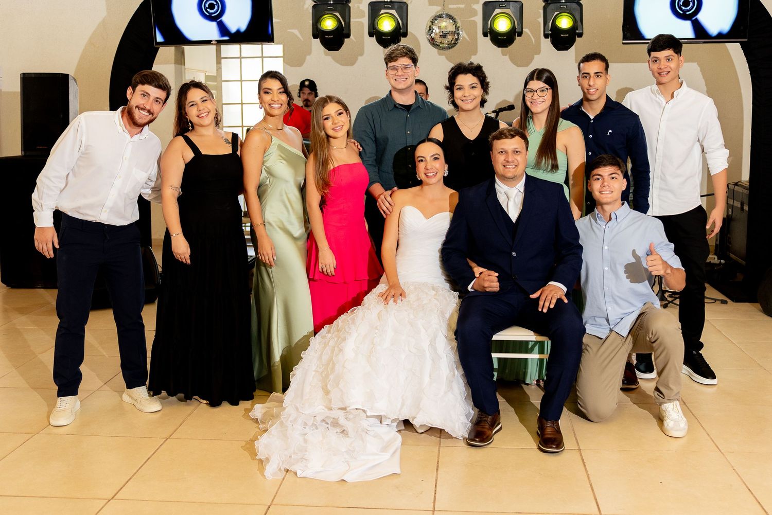 Group photo at a wedding reception with bride in white gown surrounded by elegantly dressed family and friends.