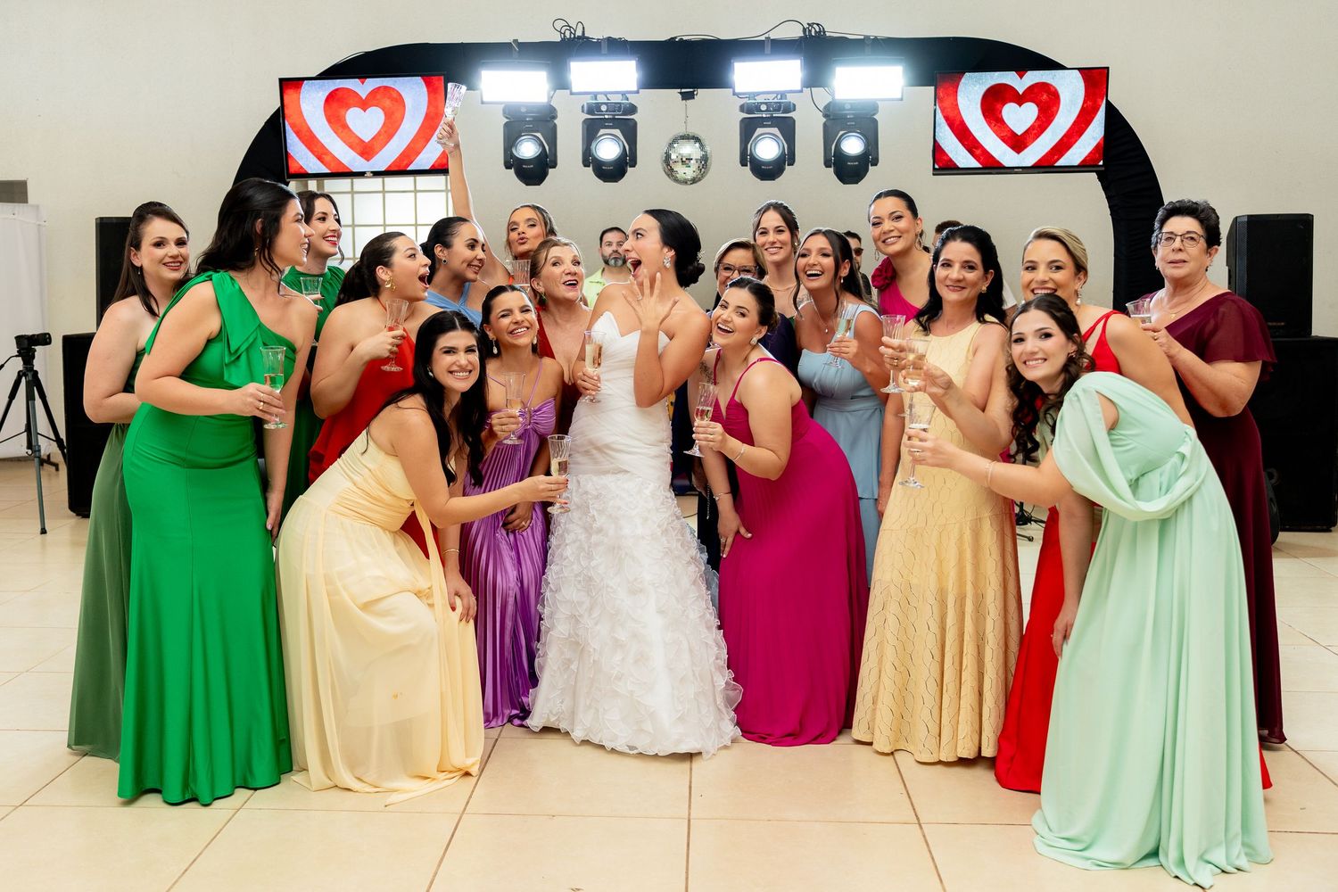 Bride in white gown poses with colorful bridesmaids in rainbow dresses at a festive wedding reception.