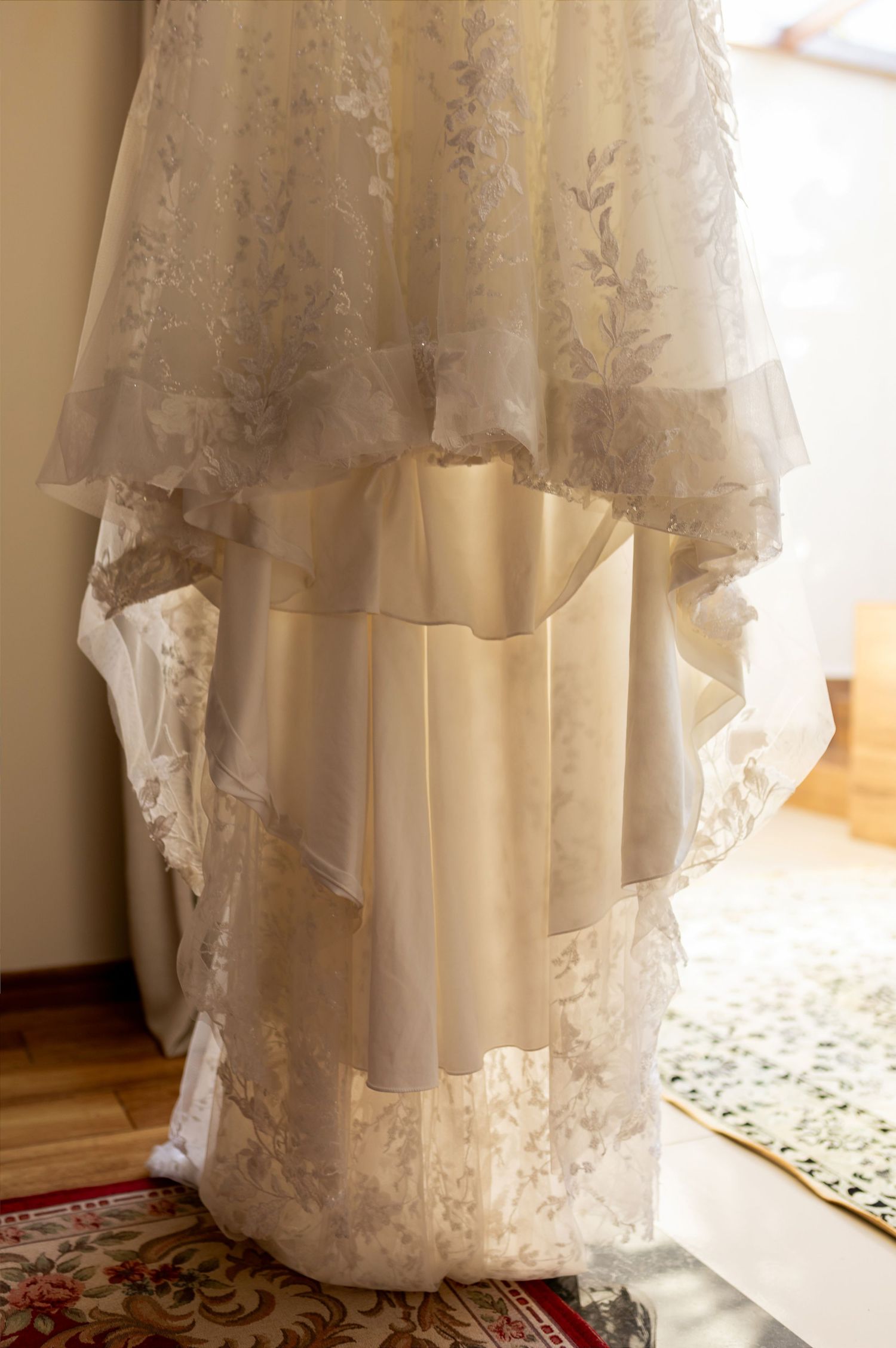 Elegant white lace wedding dress hanging, featuring layered skirt with floral lace details and soft ivory fabric.