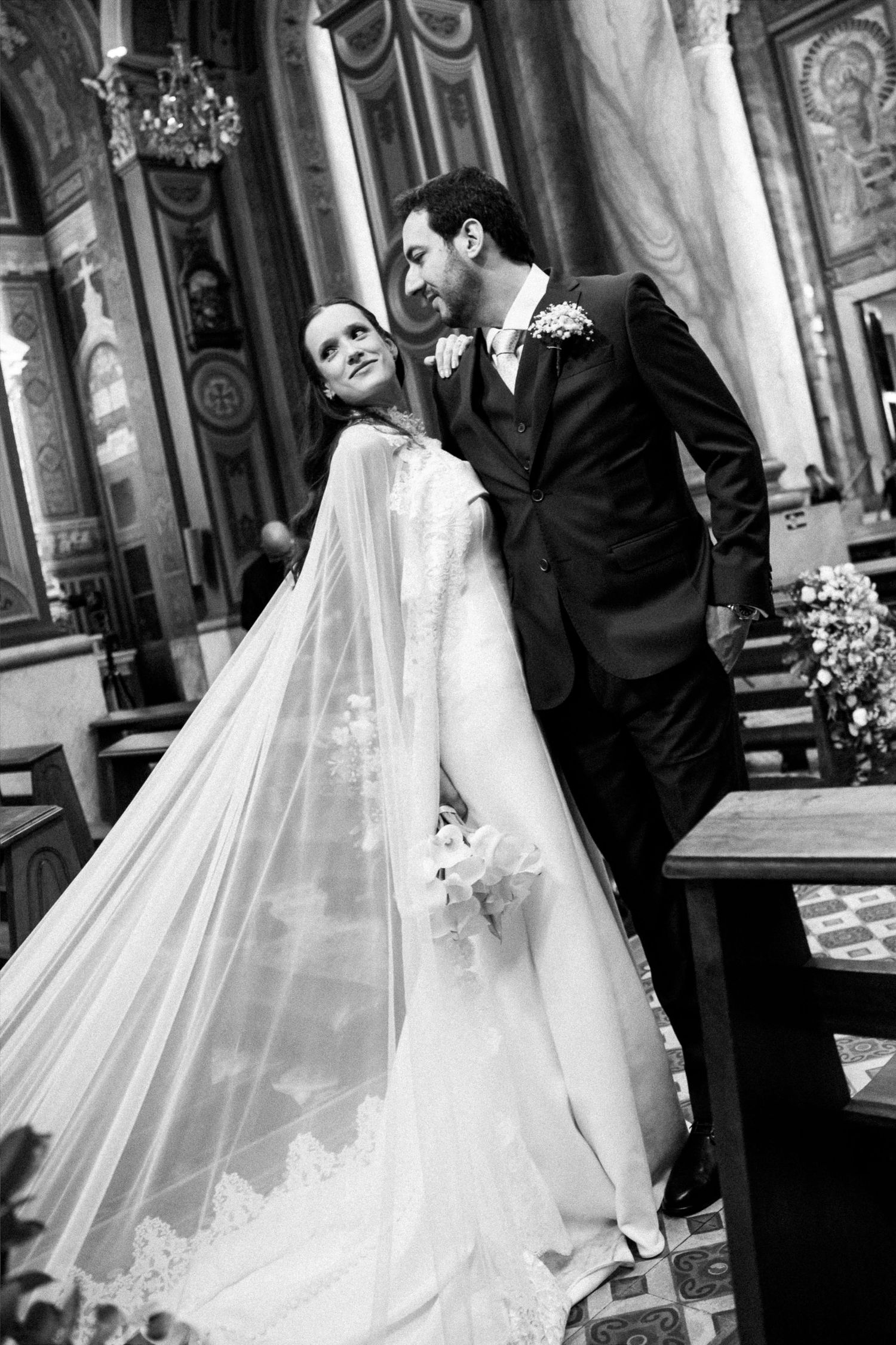 Black and white wedding photo of bride and groom sharing a romantic moment inside an ornate church.