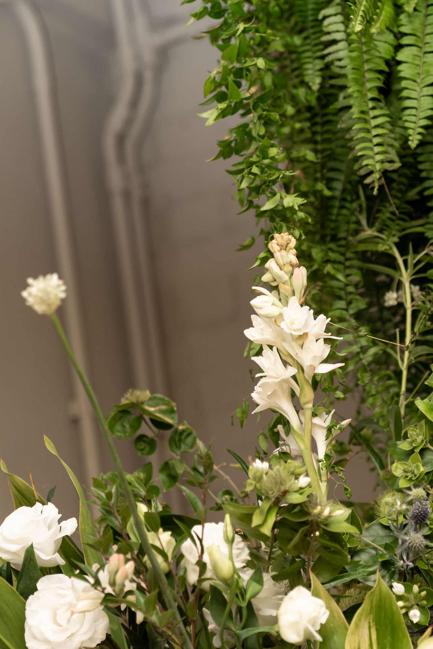 Elegant white floral arrangement with roses, tuberose, and lush green ferns for a sophisticated wedding decor display.