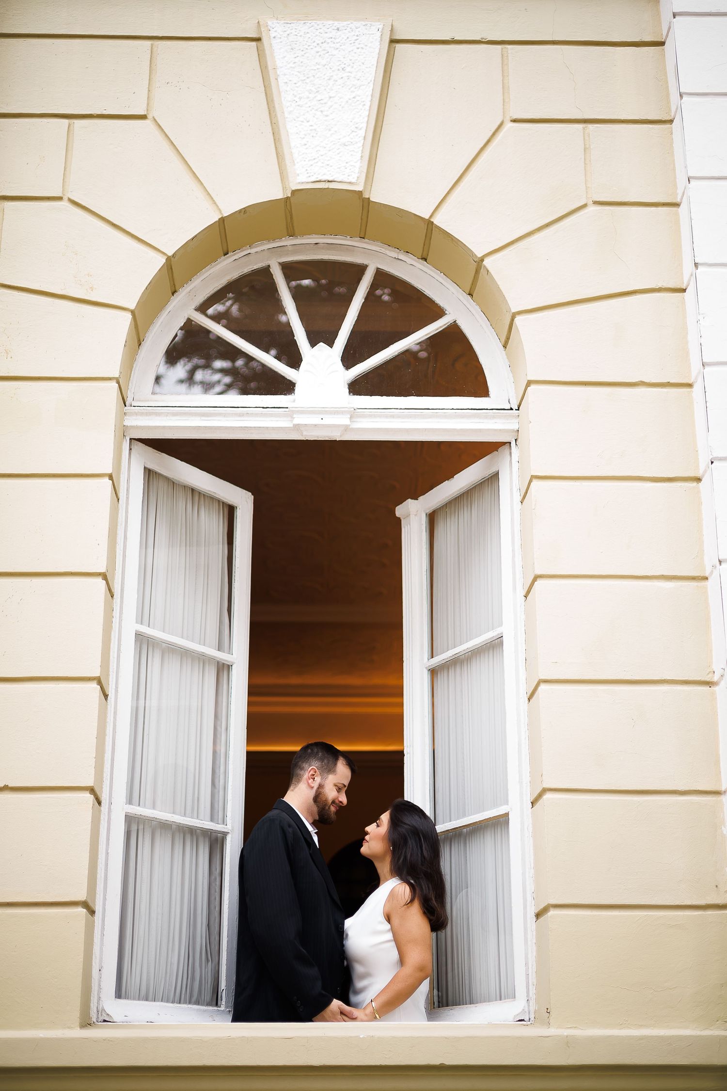 Bride and groom stand facing each other in an elegant arched doorway at sunset, framed by white French doors.