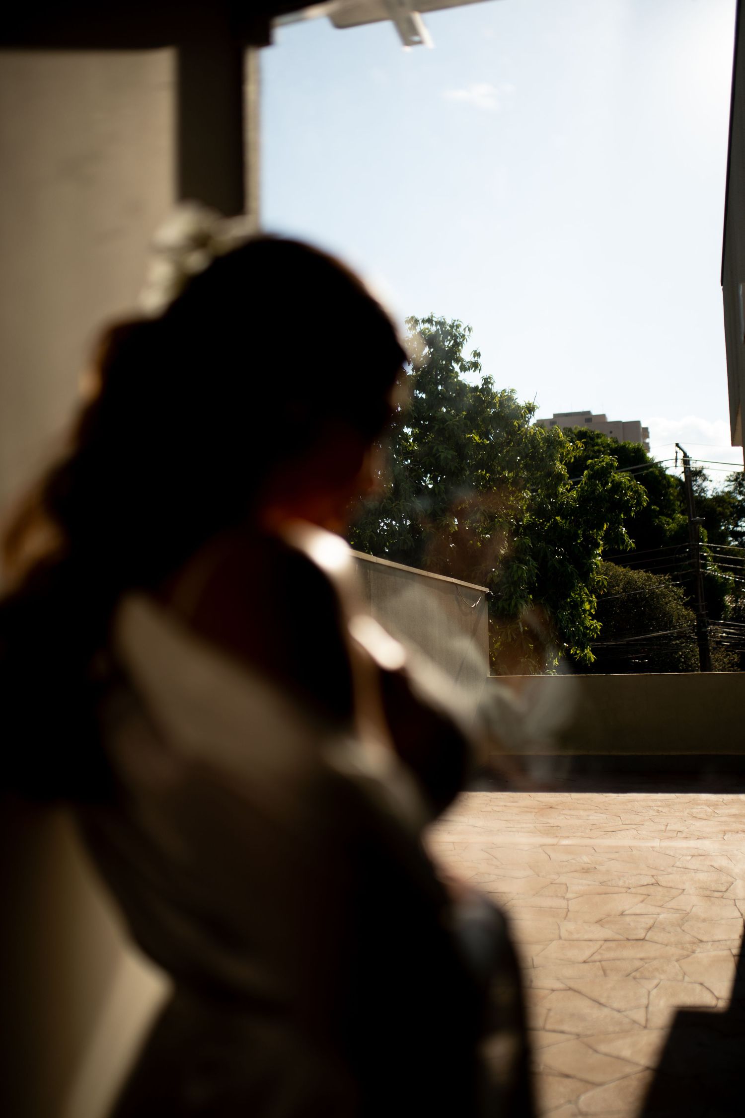 Silhouette of a bride in a white dress standing by an open doorway with sunlit green trees in the background.