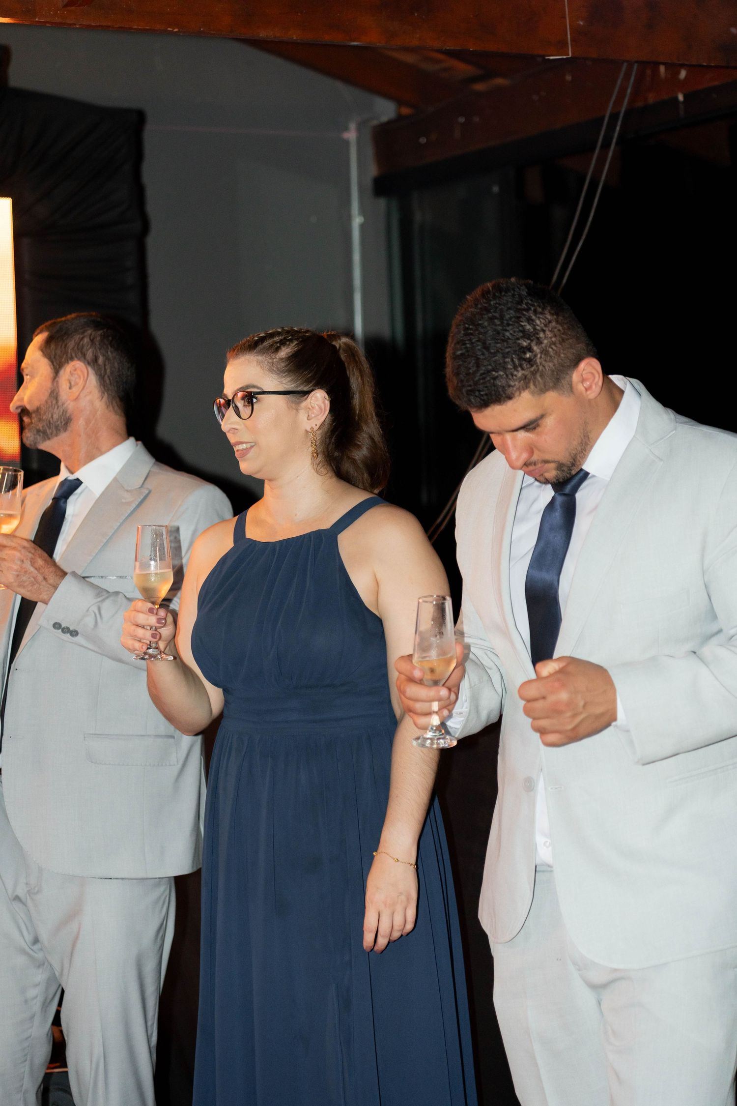 Wedding guests in formal attire hold champagne glasses at evening reception celebration.