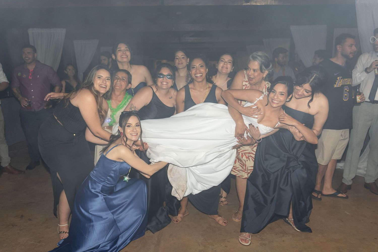 Group of women celebrating at a wedding reception, lifting the bride in her white gown while smiling and posing together.